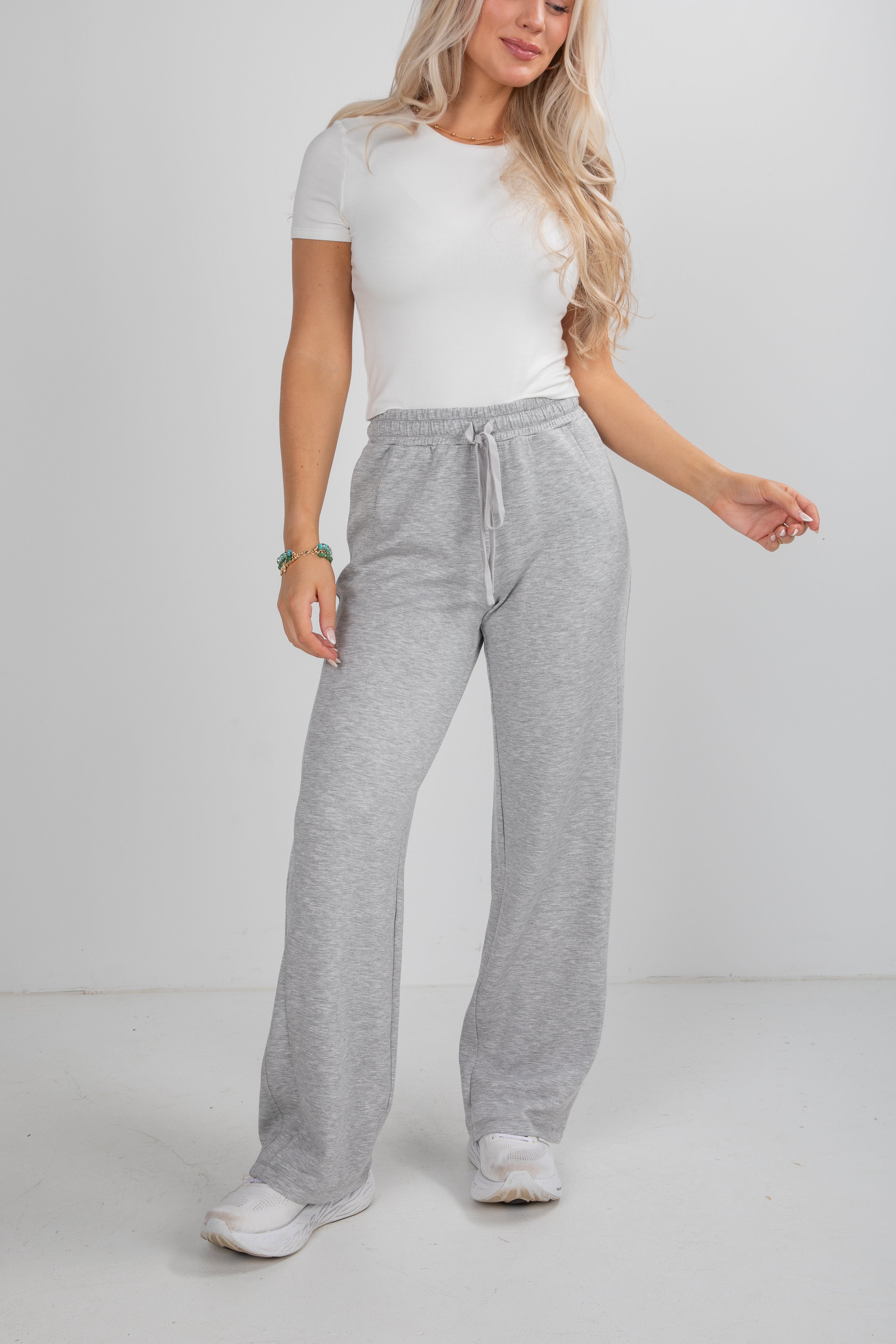Woman wearing a white t-shirt and gray sweatpants on a plain background
