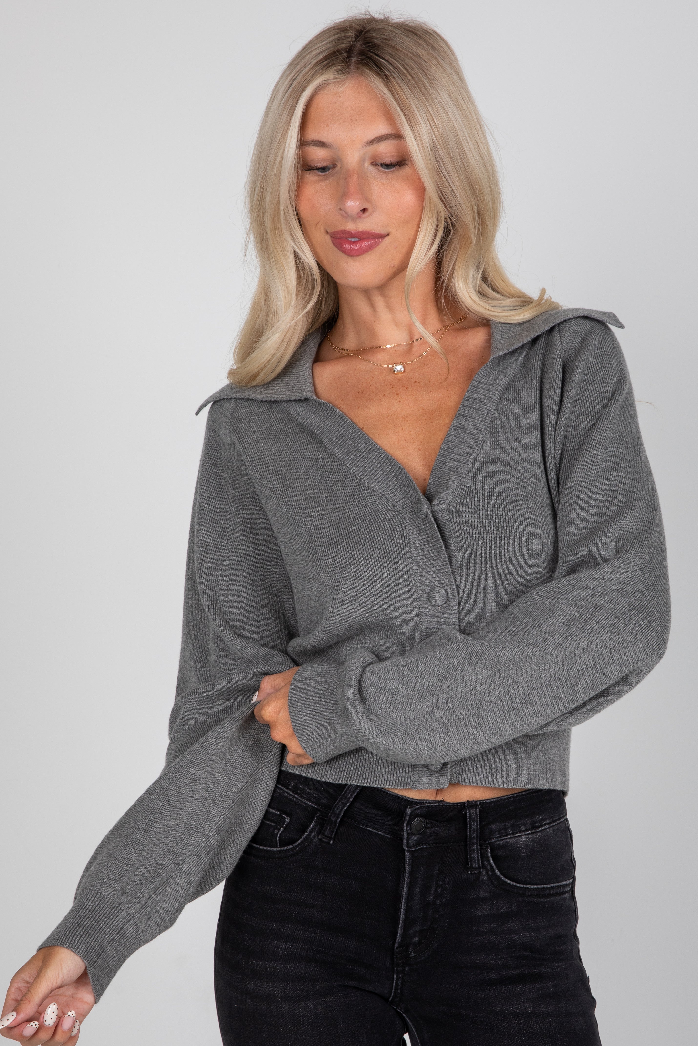 Woman wearing a gray cropped cardigan and black jeans on a plain background