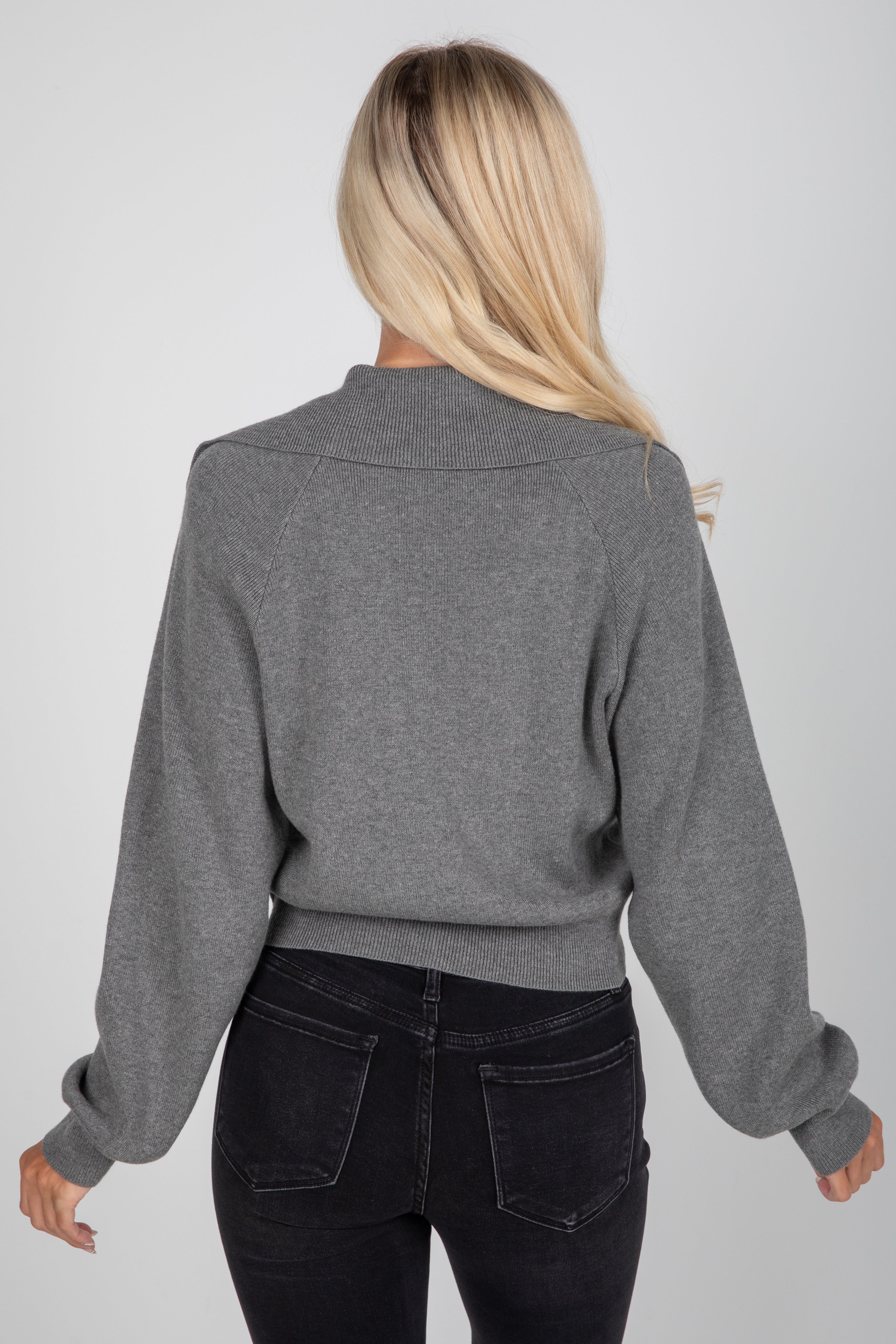 Person wearing a gray sweater and black pants on a plain background