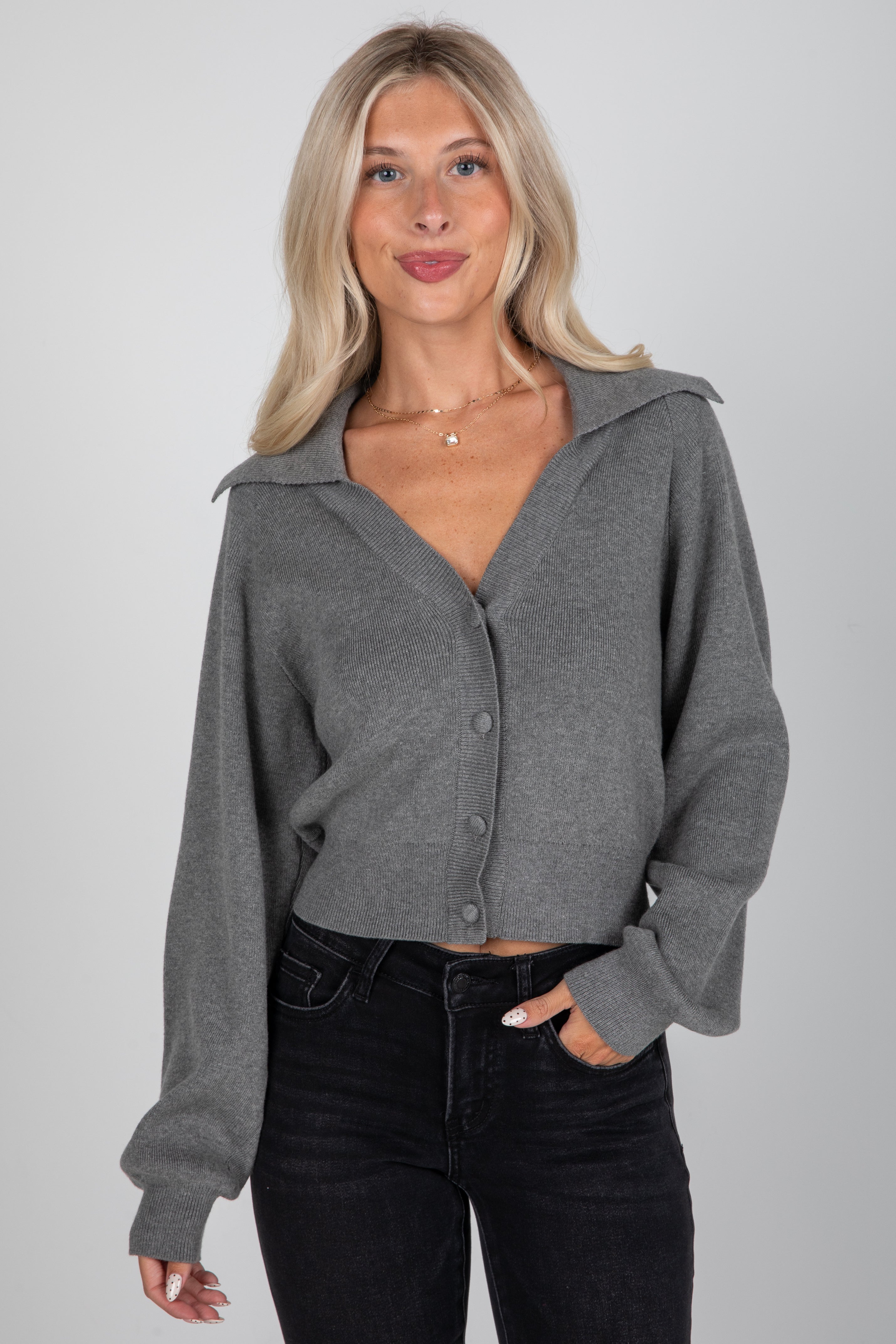 Woman wearing a gray button-up shirt and black pants on a plain background