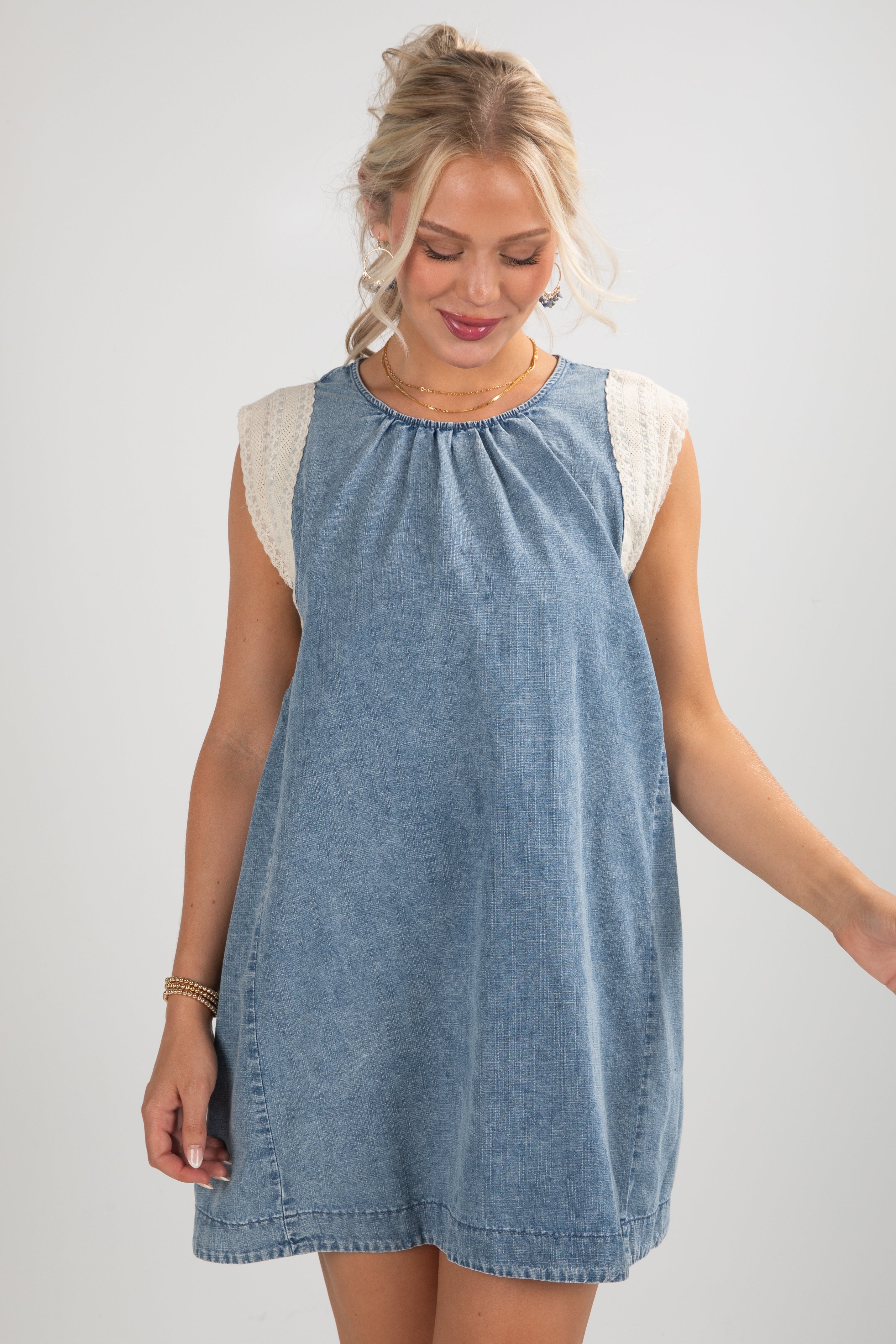 Woman wearing a blue denim dress with white lace sleeves on a plain background