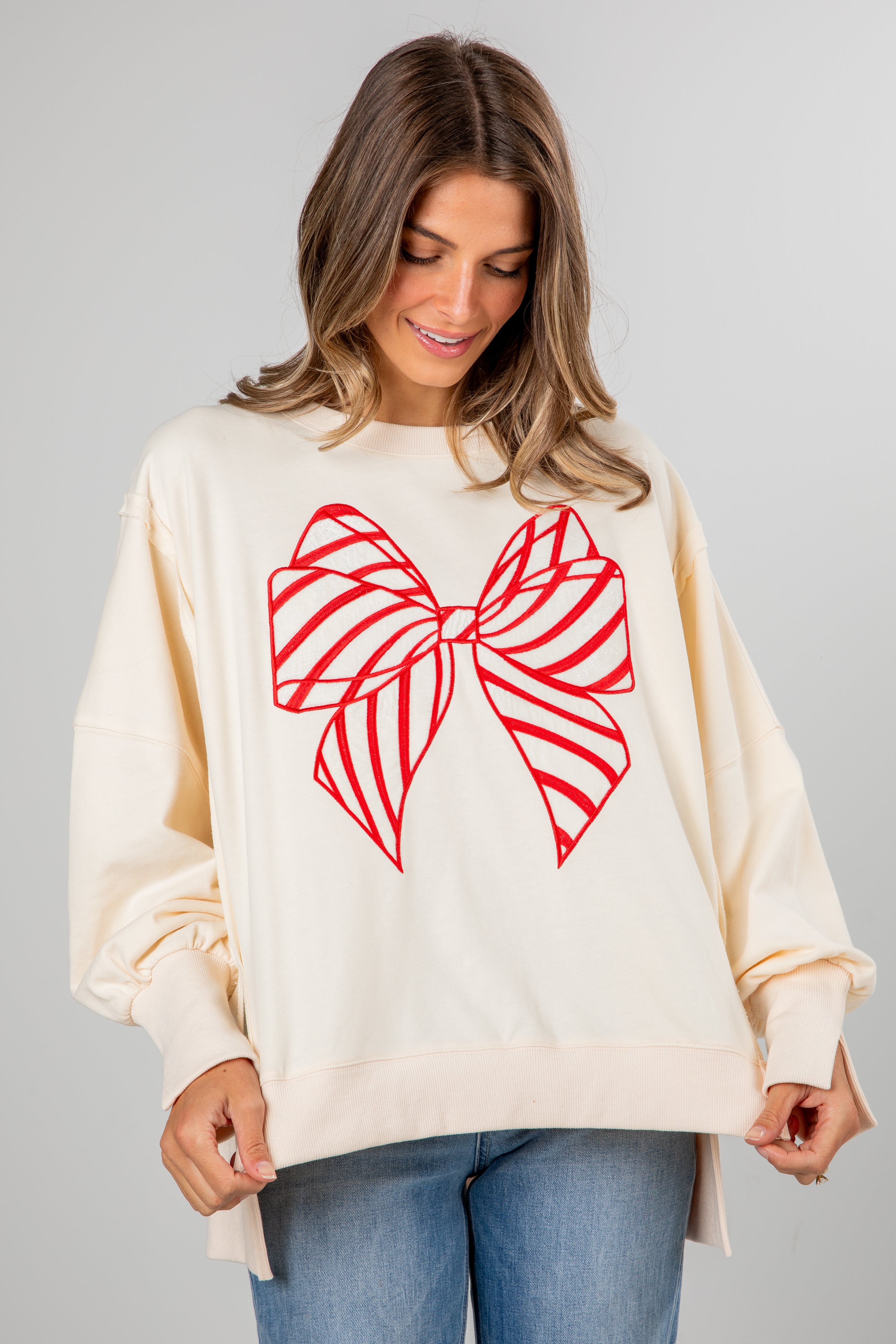Woman wearing a cream sweater with a red bow design on a gray background