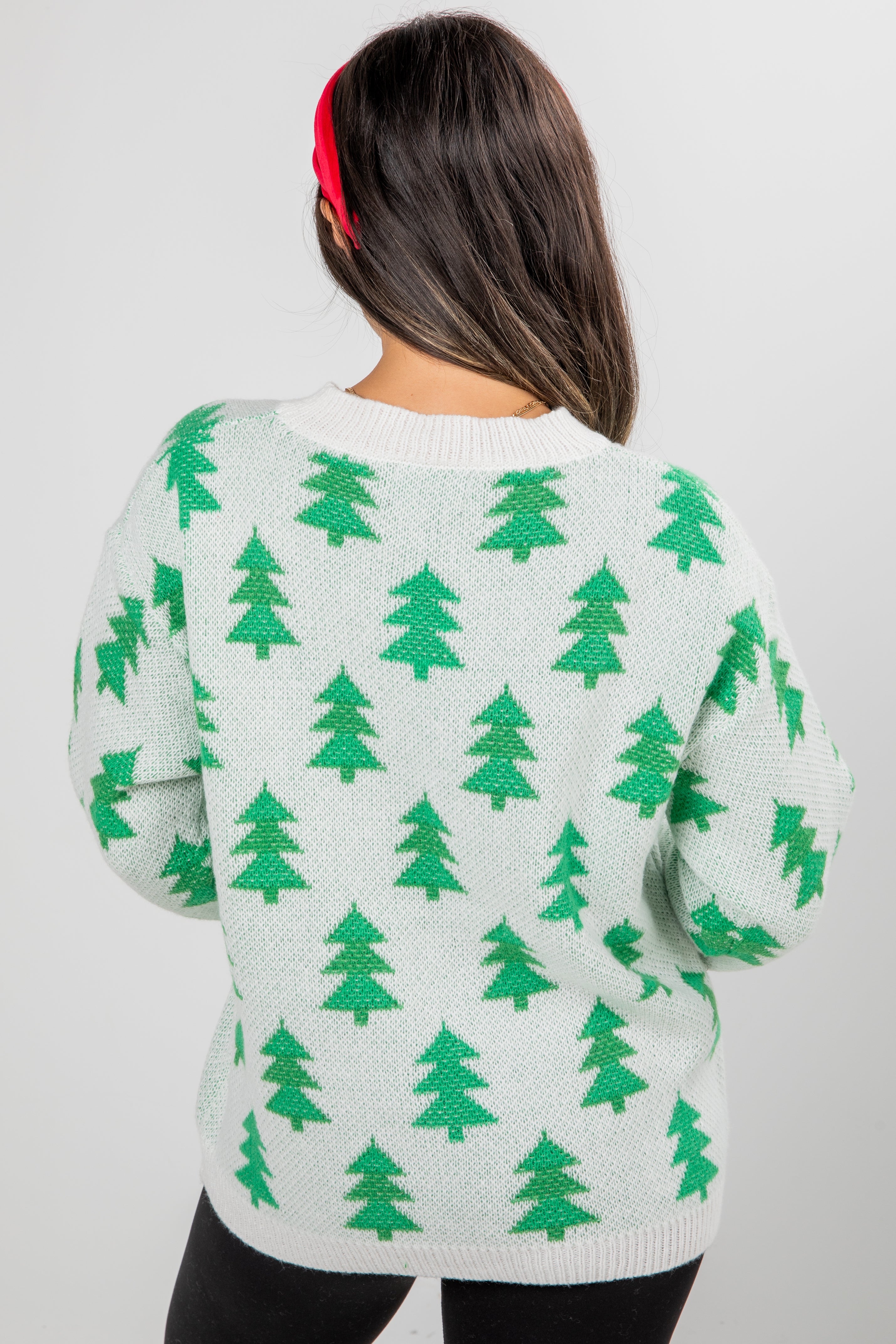 Person wearing a light green sweater with green tree patterns on a plain background