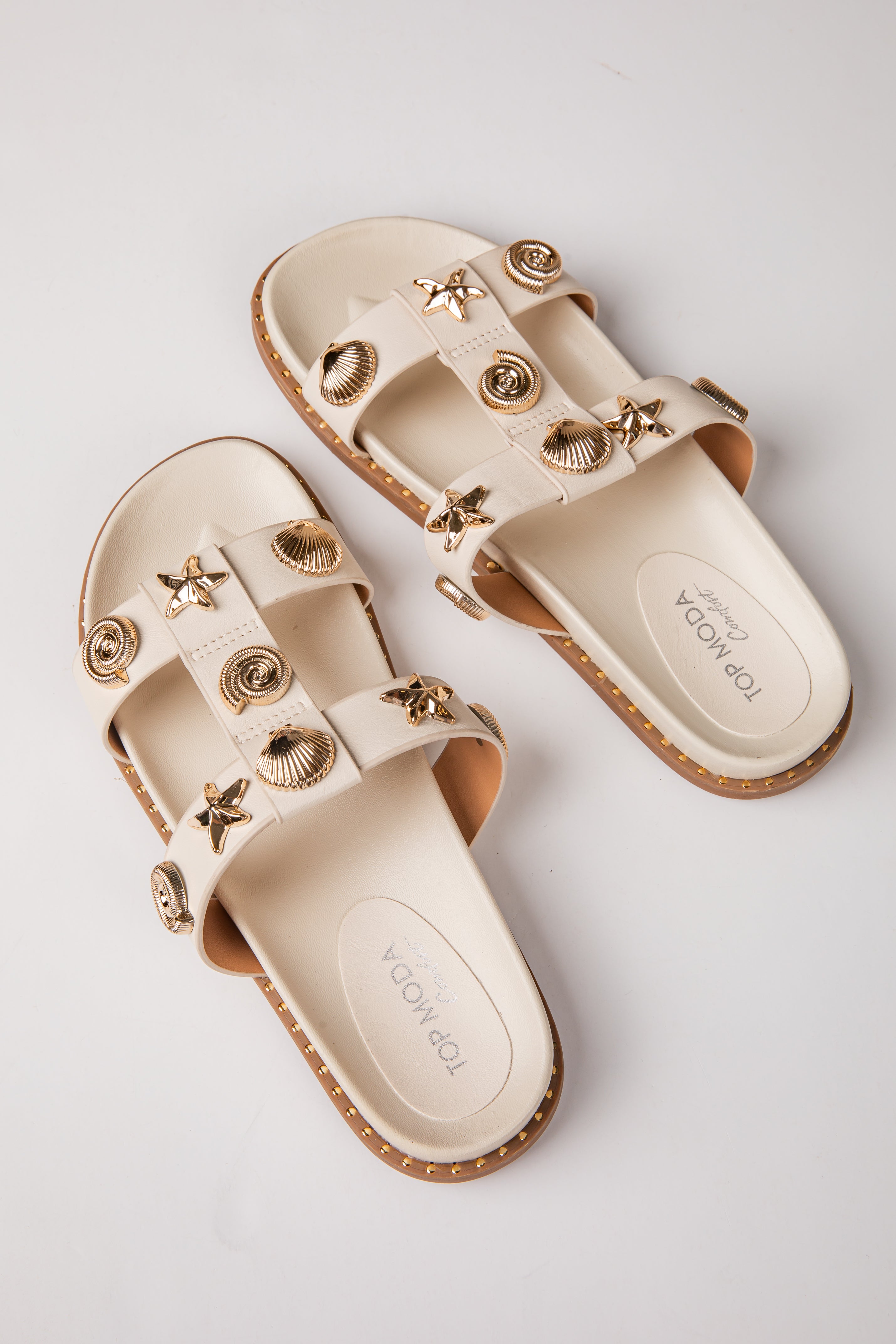 Pair of beige sandals with gold embellishments on a light gray background