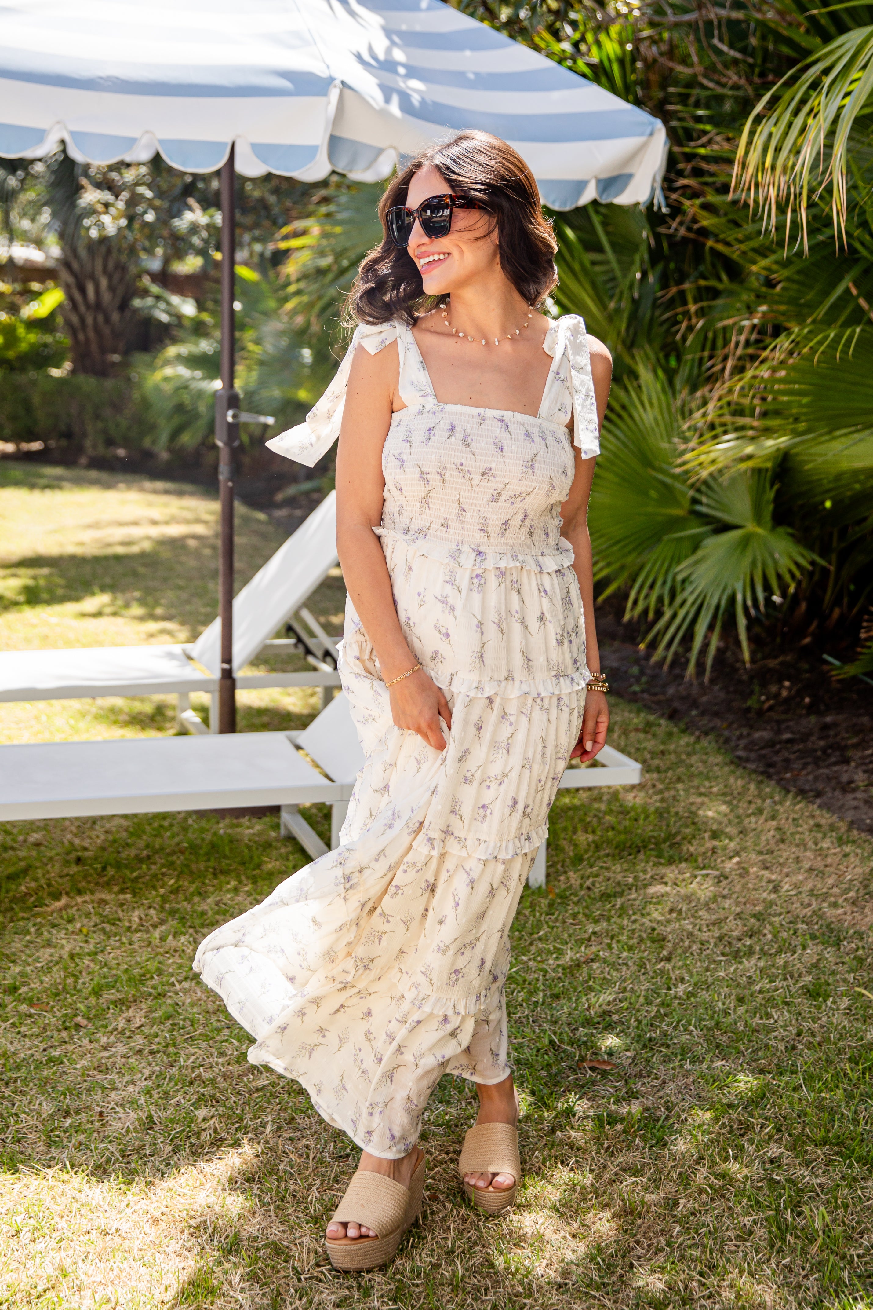 Woman in a white lace dress standing outdoors under a striped canopy.