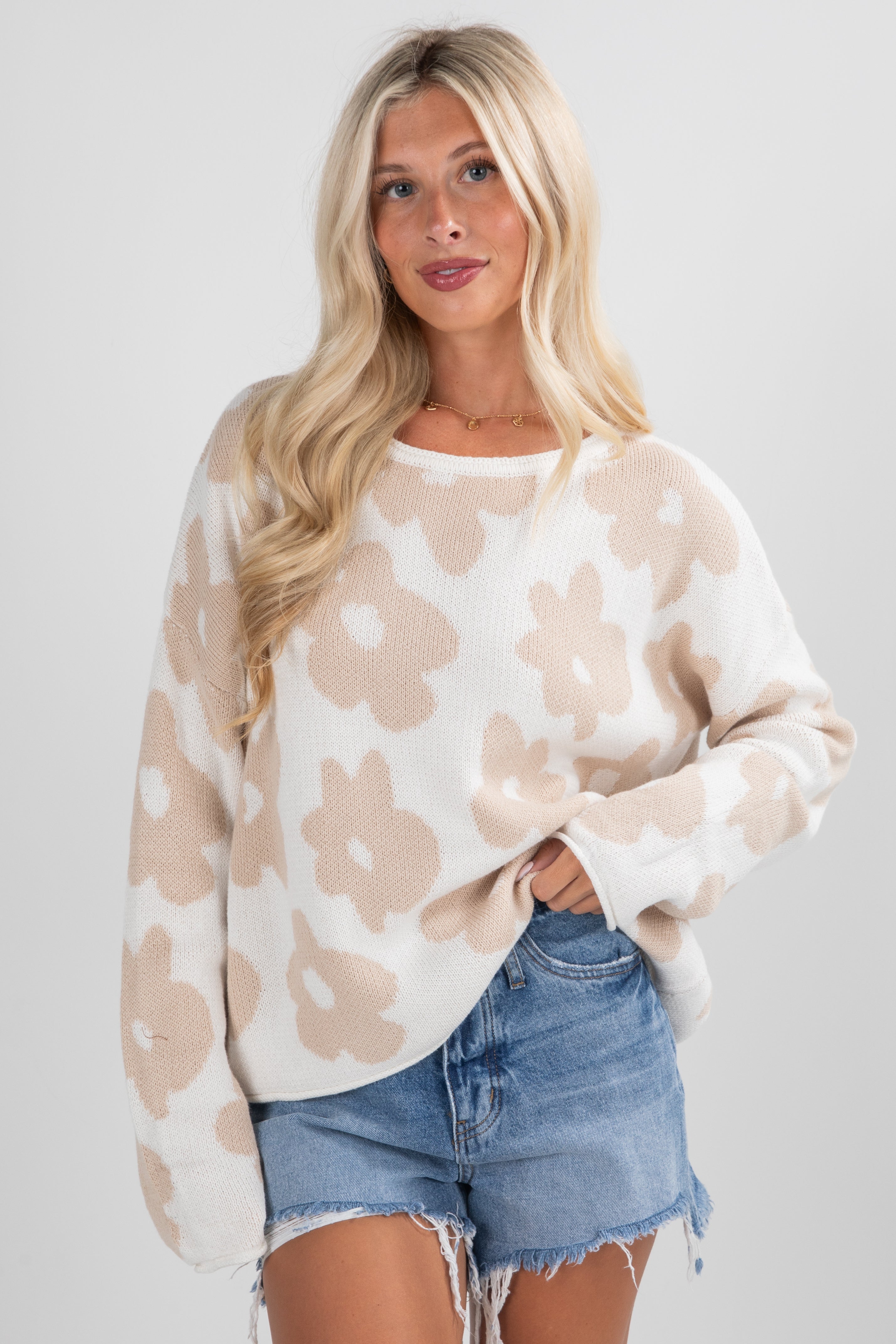 Woman wearing a beige and white patterned sweater with denim shorts on a plain background