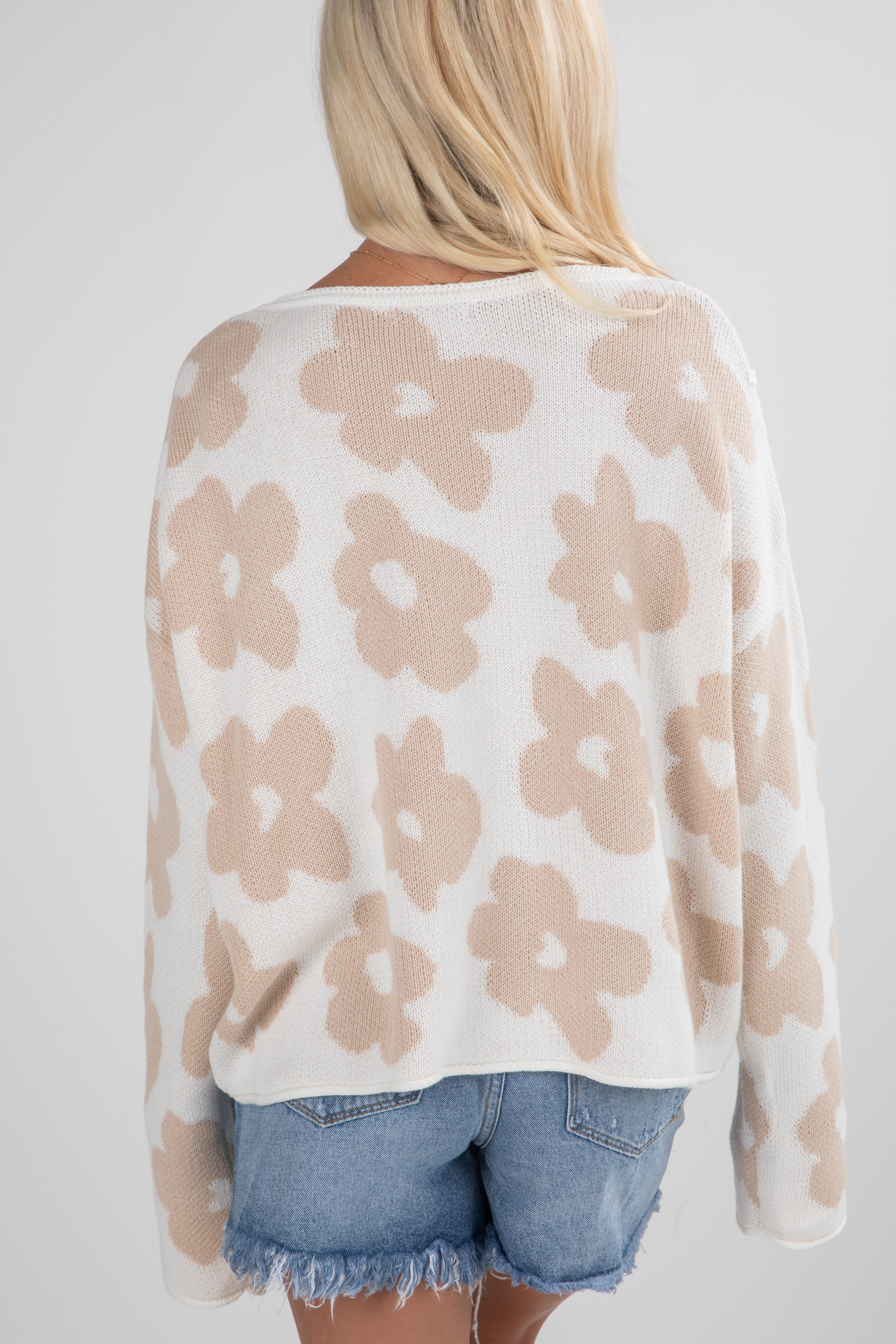 Woman wearing a beige floral-patterned sweater and denim shorts on a white background