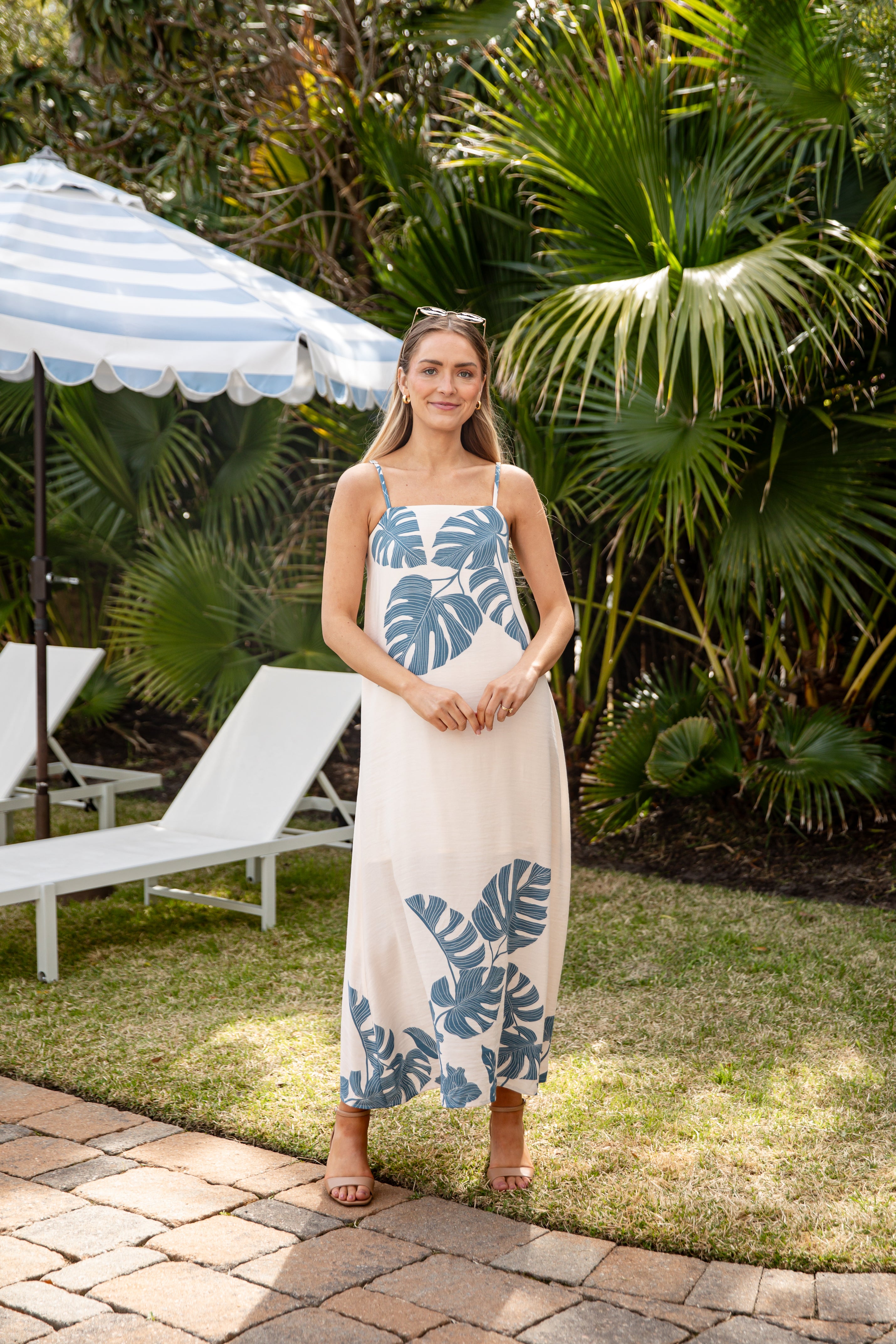 Woman in a floral dress standing in a garden with palm trees and lounge chairs.