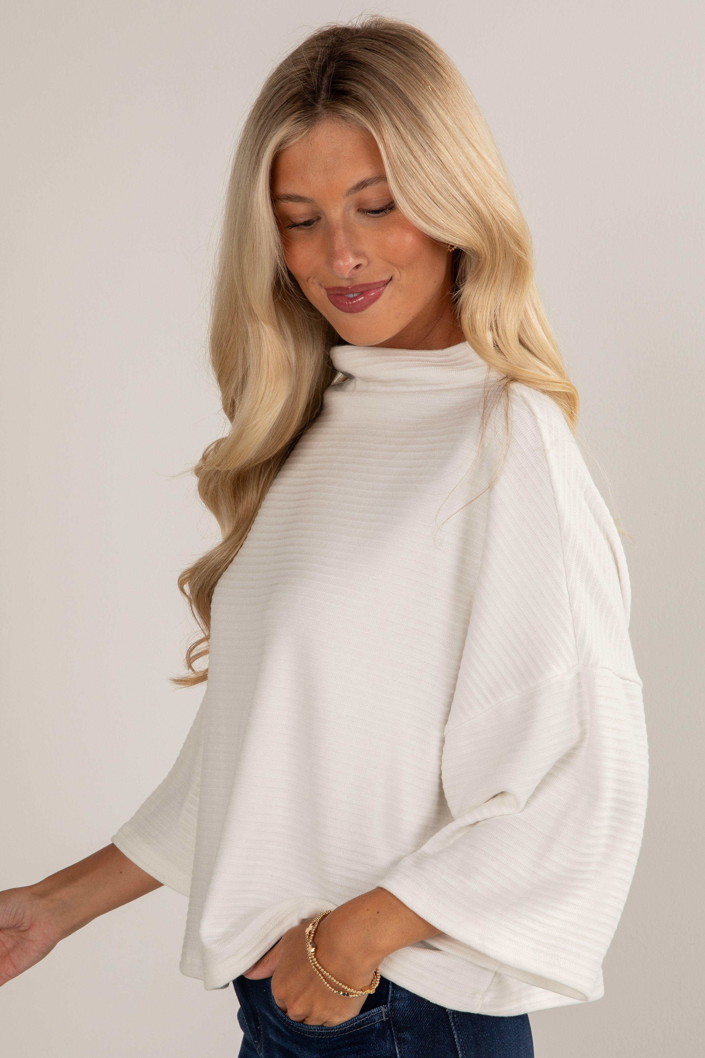 Woman wearing a white long-sleeve top against a plain background