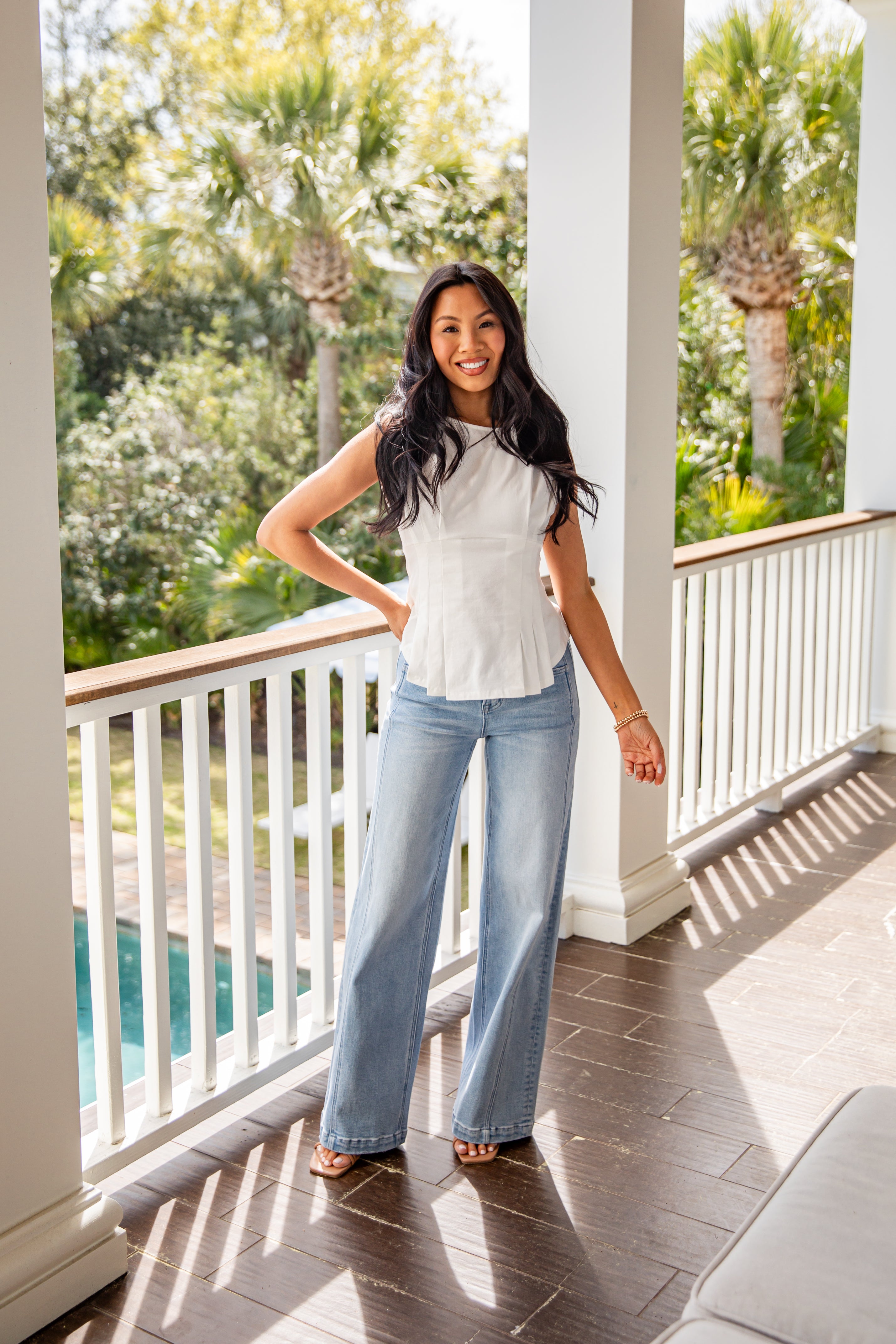 Woman standing on a porch with a scenic view of trees and a pool.