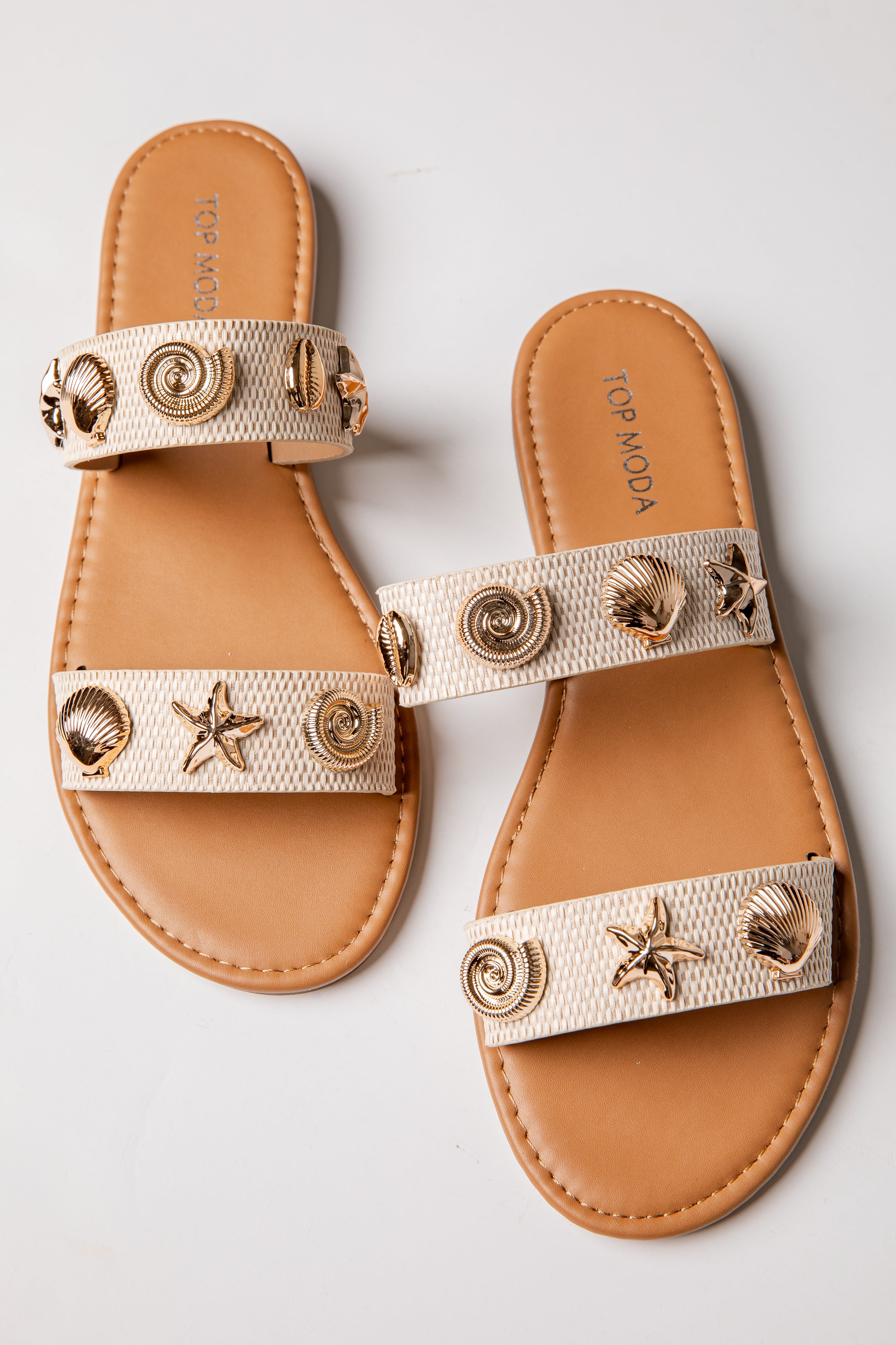 Pair of tan sandals with decorative straps featuring shells and stars on a light gray background.