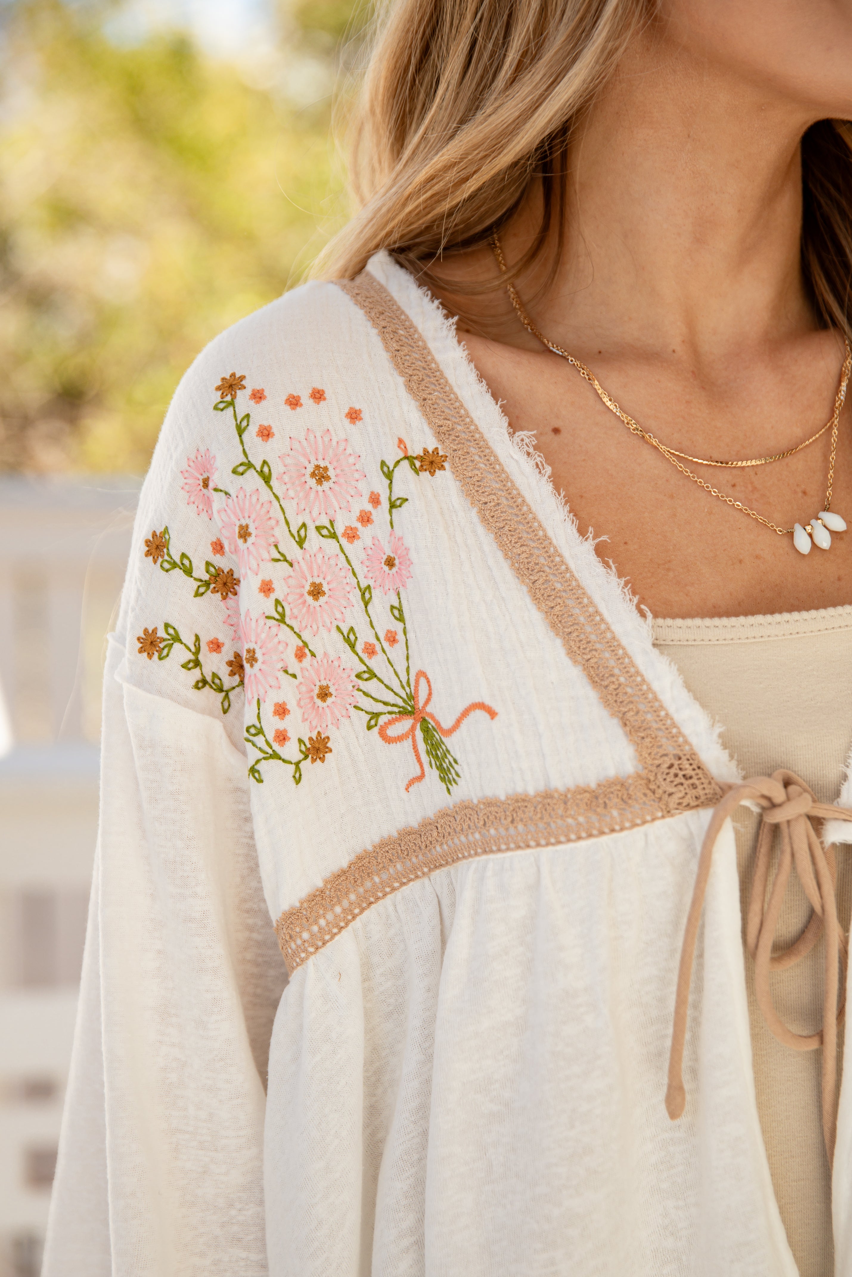 Woman wearing a white embroidered cardigan with floral designs outdoors.