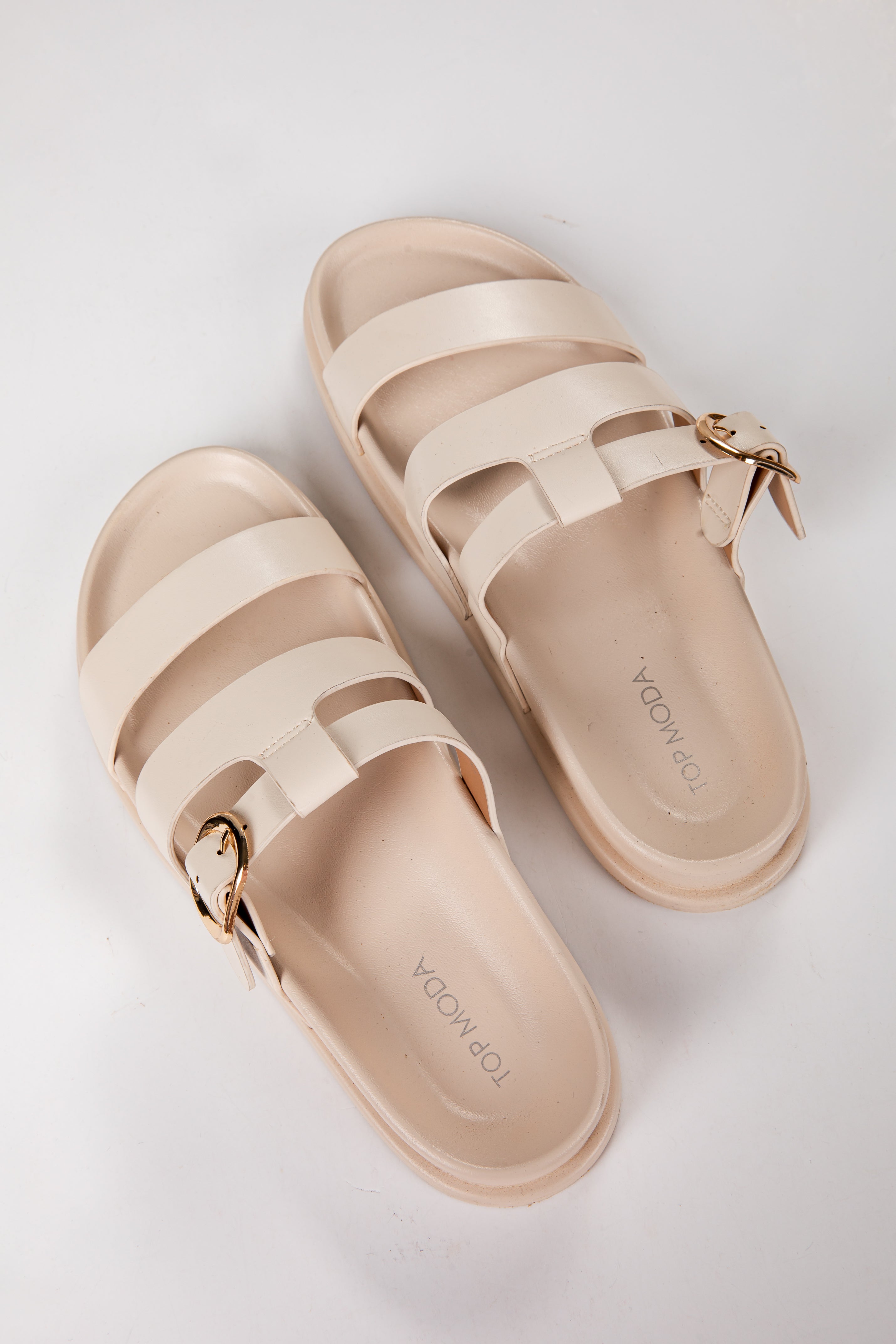 Pair of beige sandals with gold buckles on a light gray background