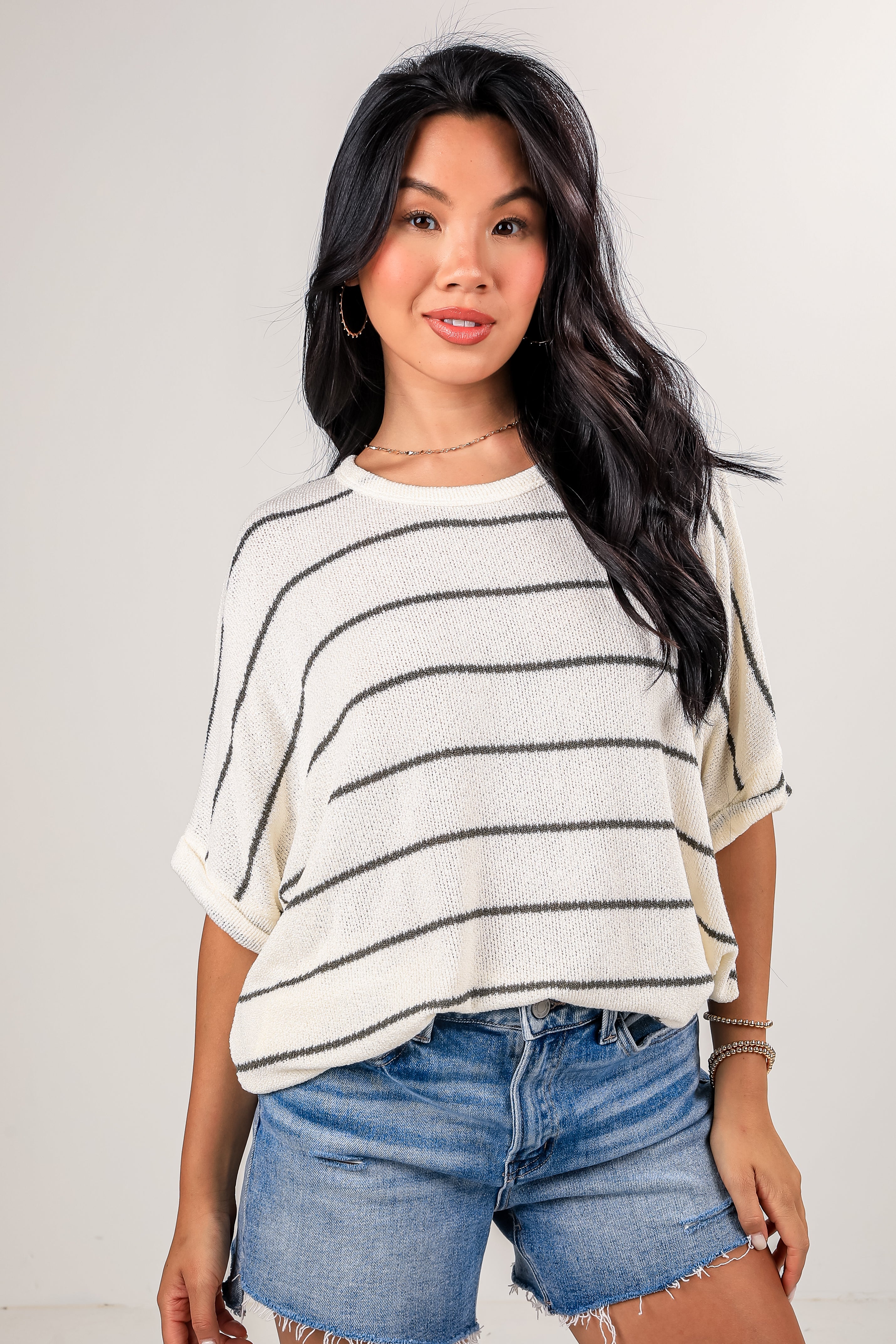Woman wearing a striped shirt and denim shorts against a plain background