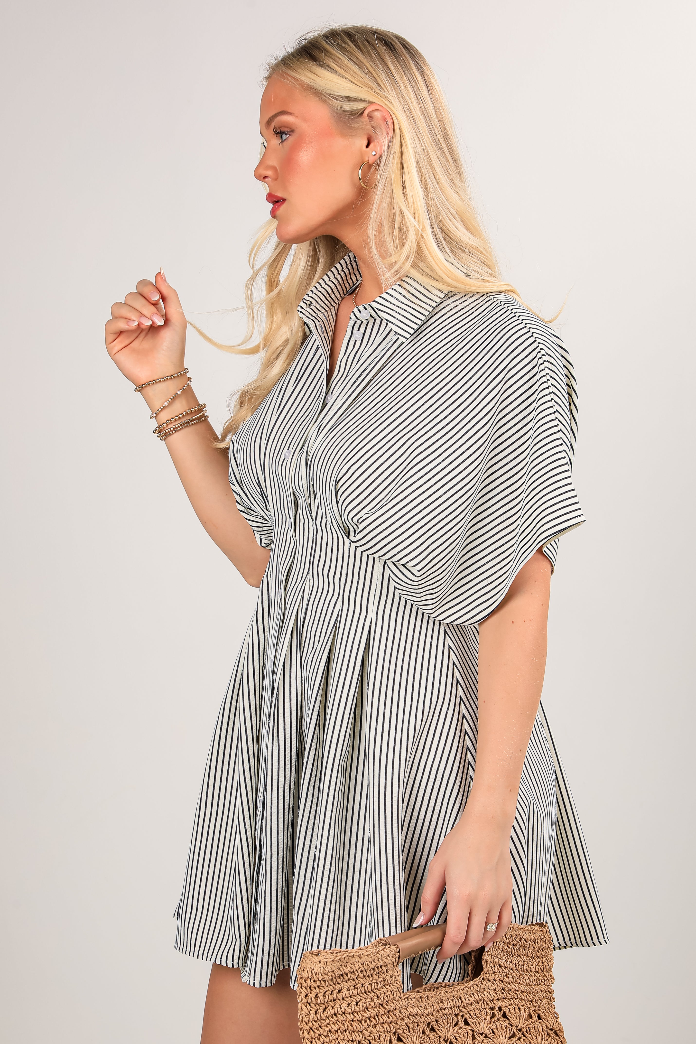Woman wearing a striped dress holding a woven bag against a plain background