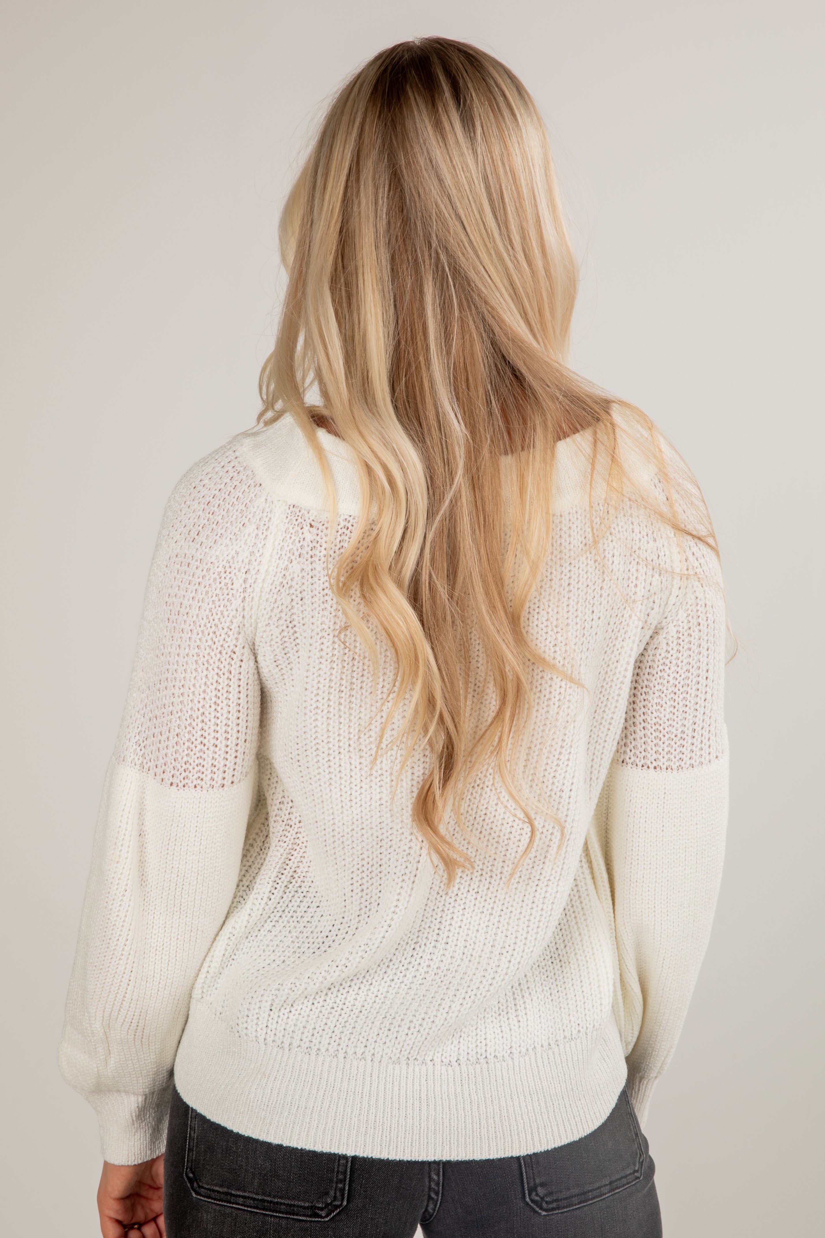Woman wearing a cream sweater with a plain background