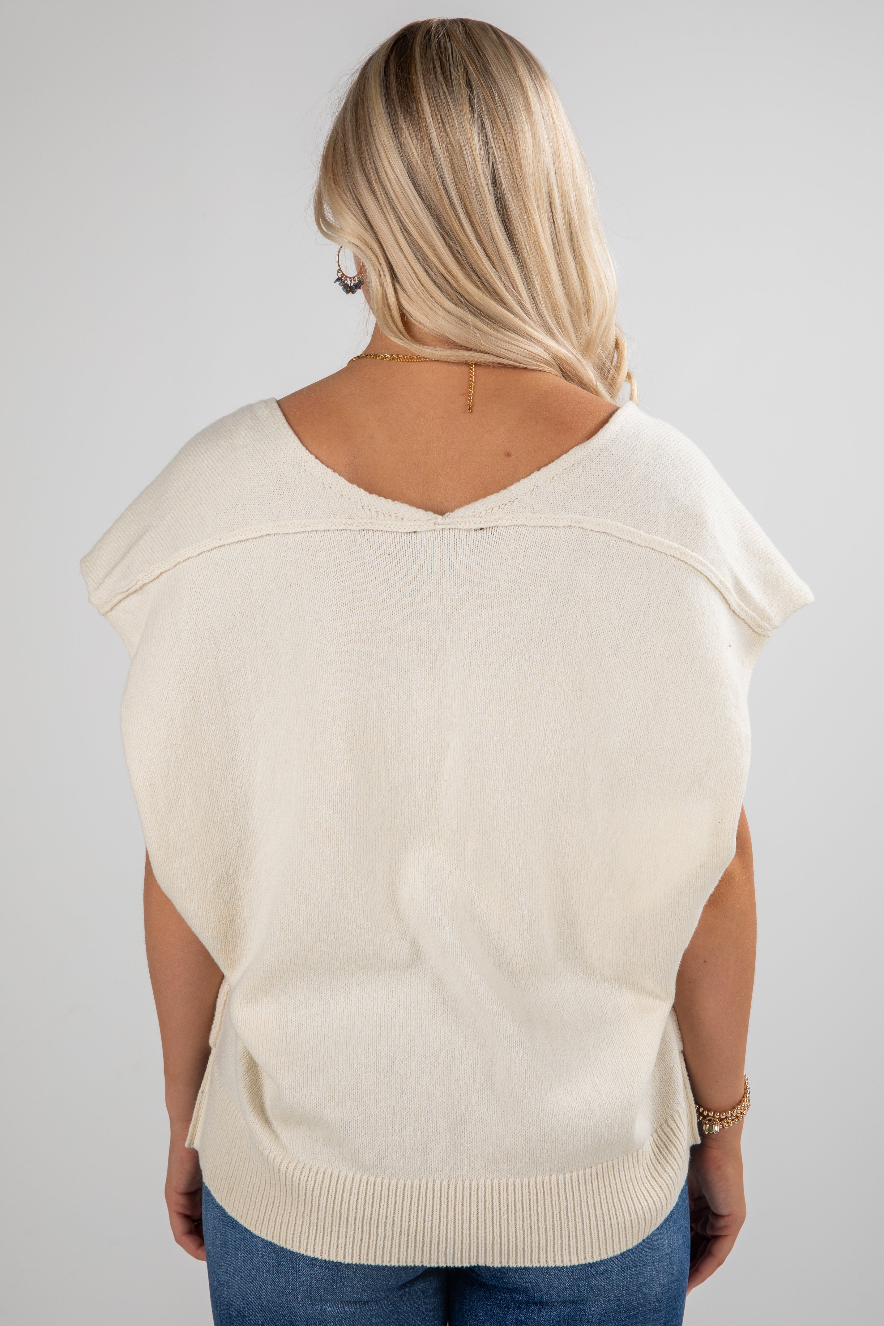 Person wearing a beige sweater vest on a plain background