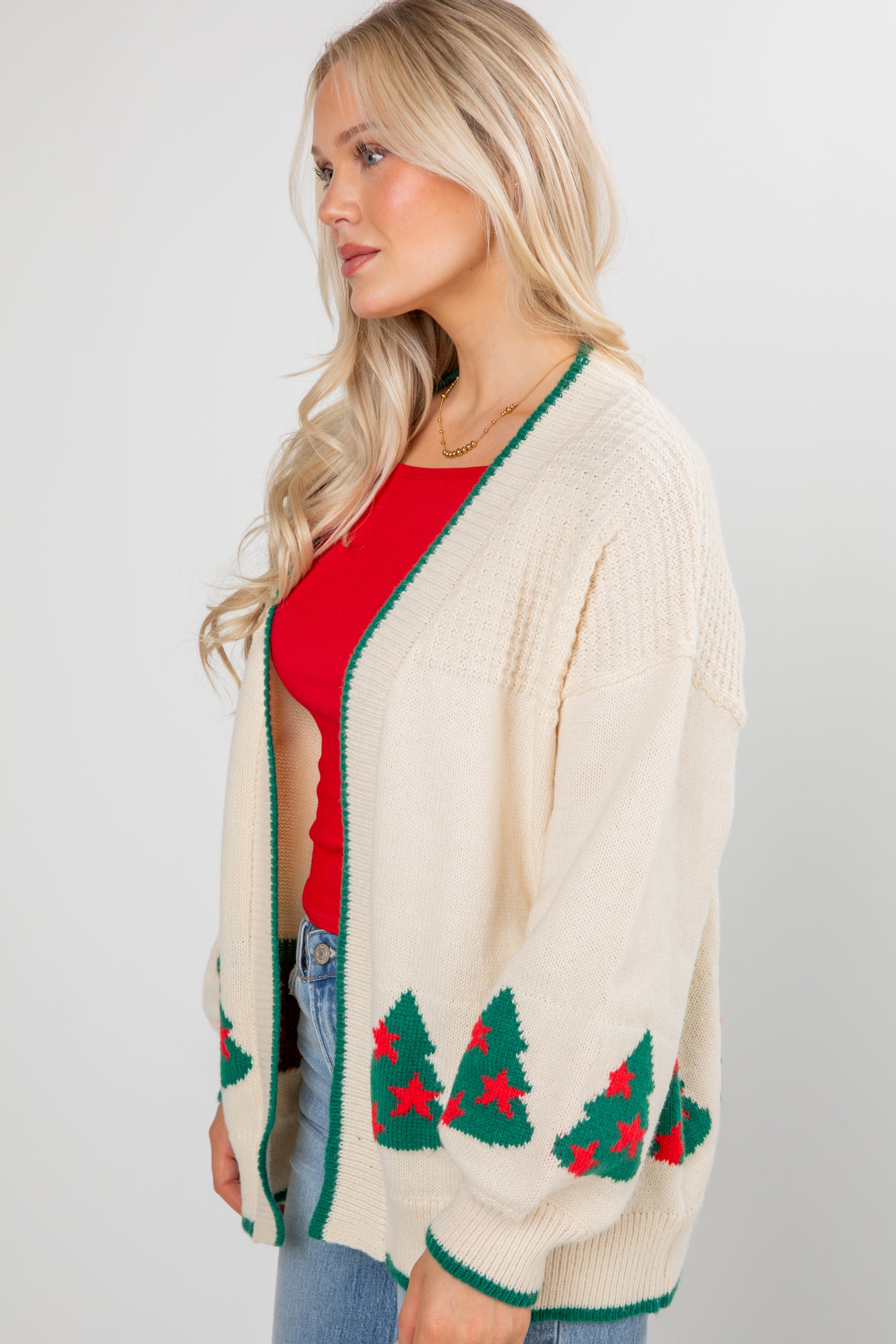 Woman wearing a cream cardigan with Christmas tree patterns on a plain background