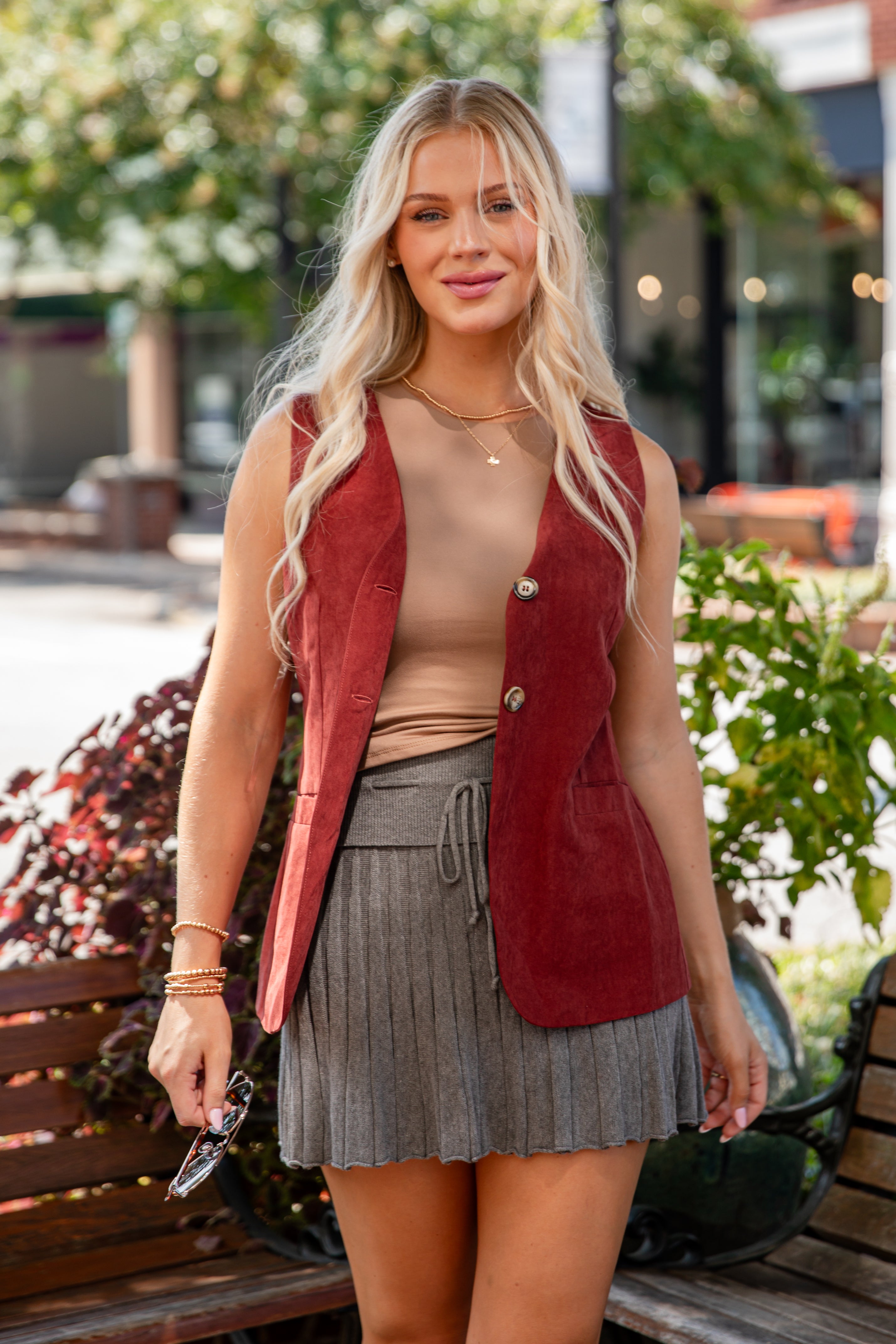 Woman wearing a red vest over a beige top and gray skirt outdoors.