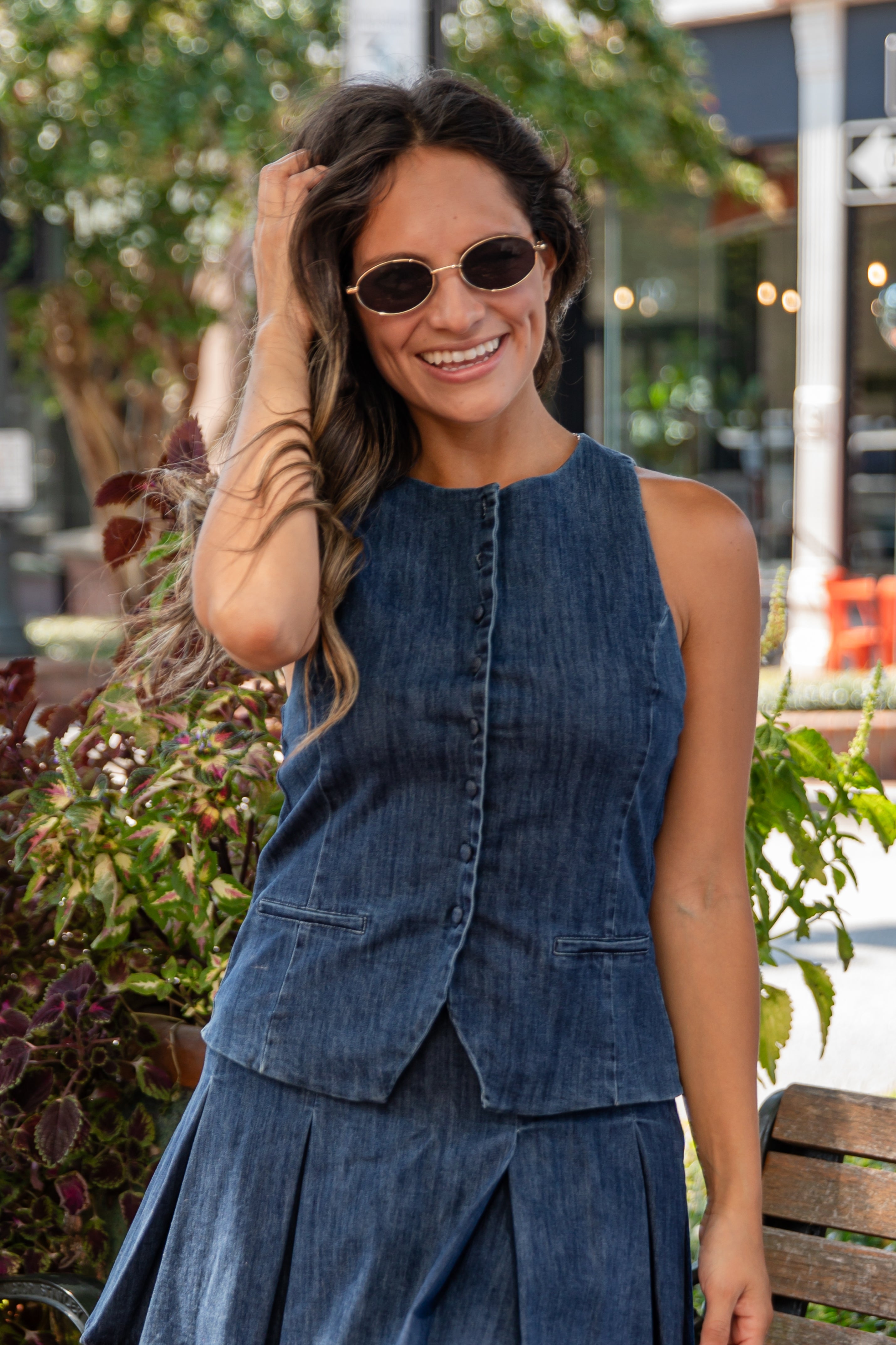 Woman wearing a blue denim outfit with sunglasses, standing outdoors.