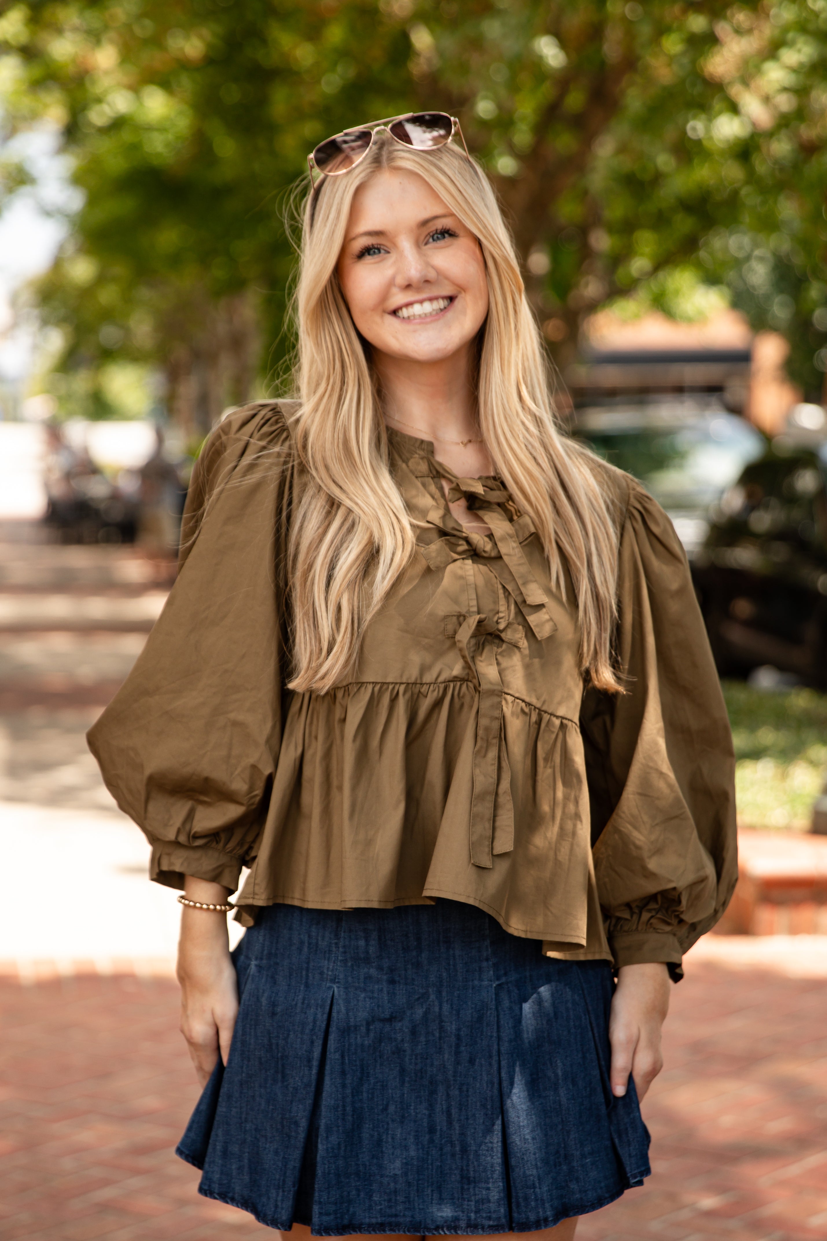 Woman wearing a brown blouse and blue skirt outdoors with trees in the background