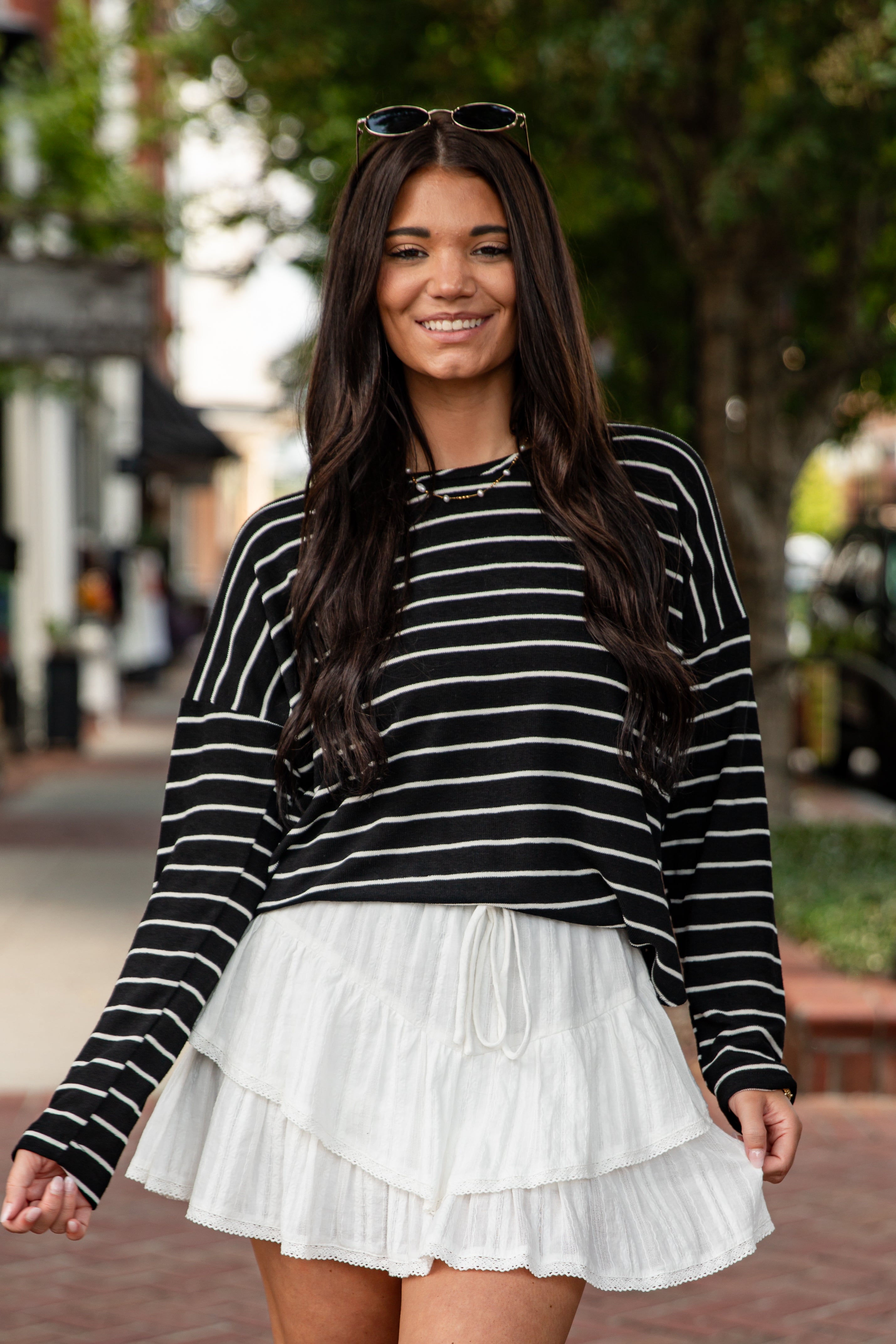 Woman wearing a black and white striped sweater and white skirt outdoors.