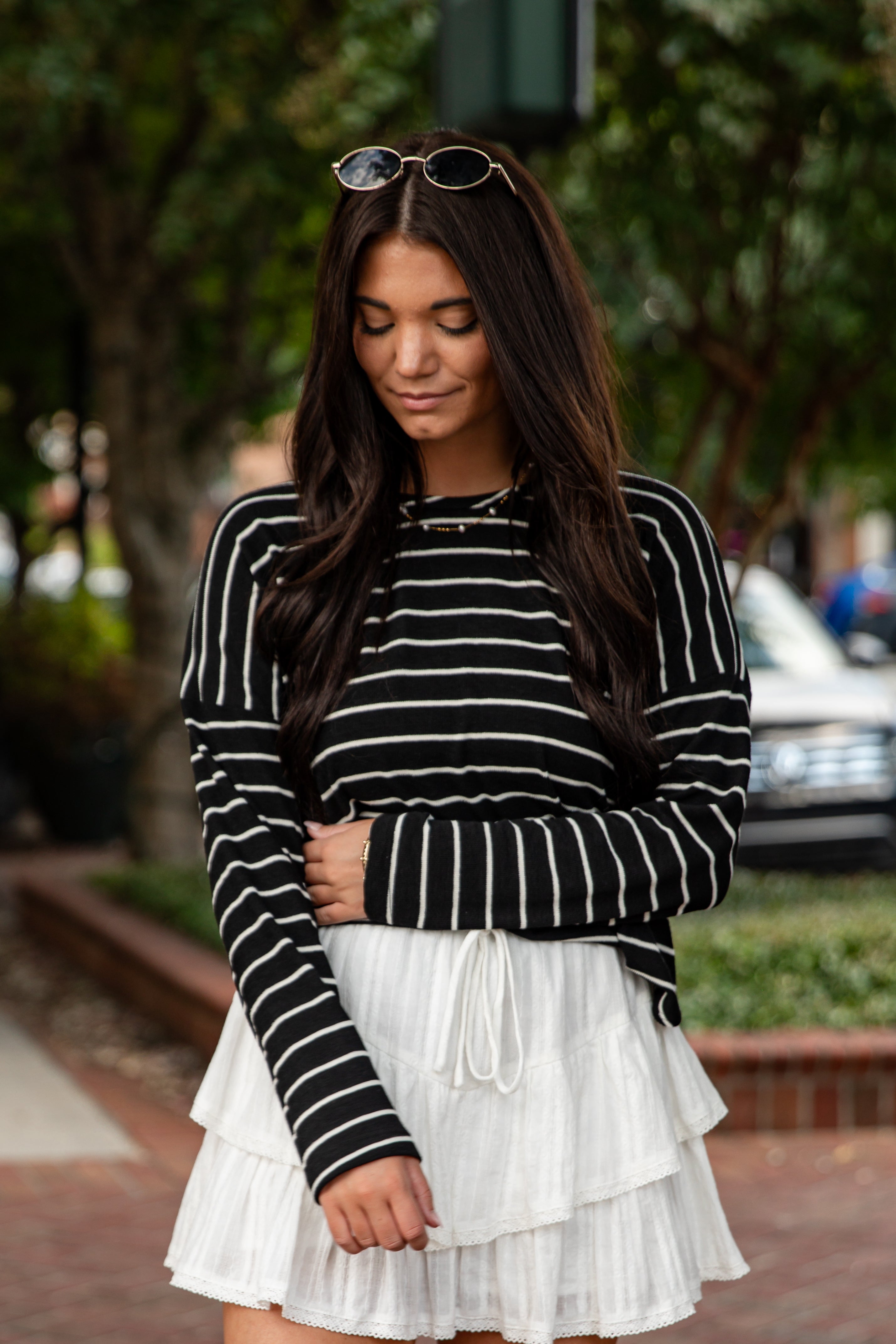 Woman wearing a black and white striped sweater and white skirt outdoors.