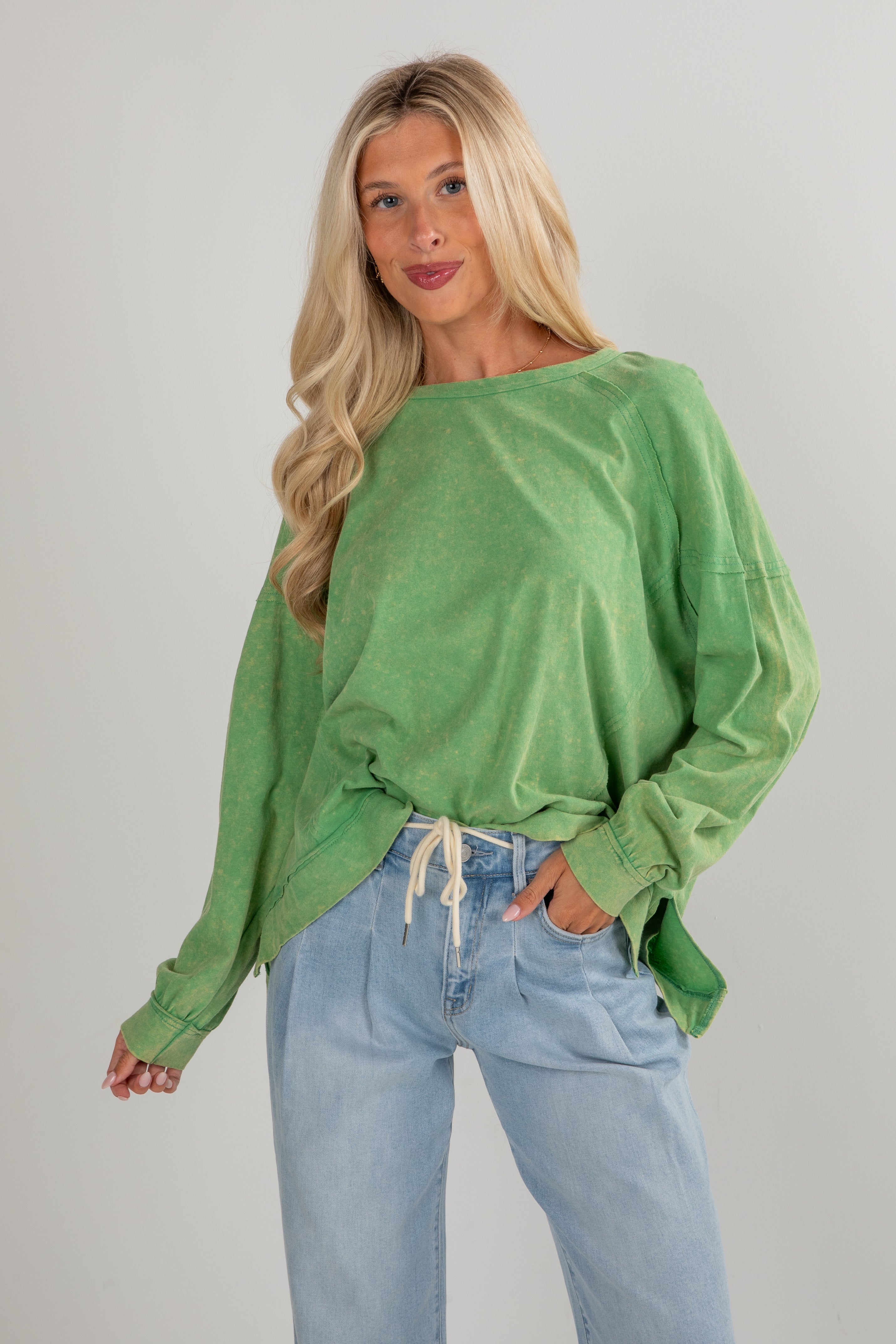 Woman wearing a green oversized sweatshirt and blue jeans against a plain background