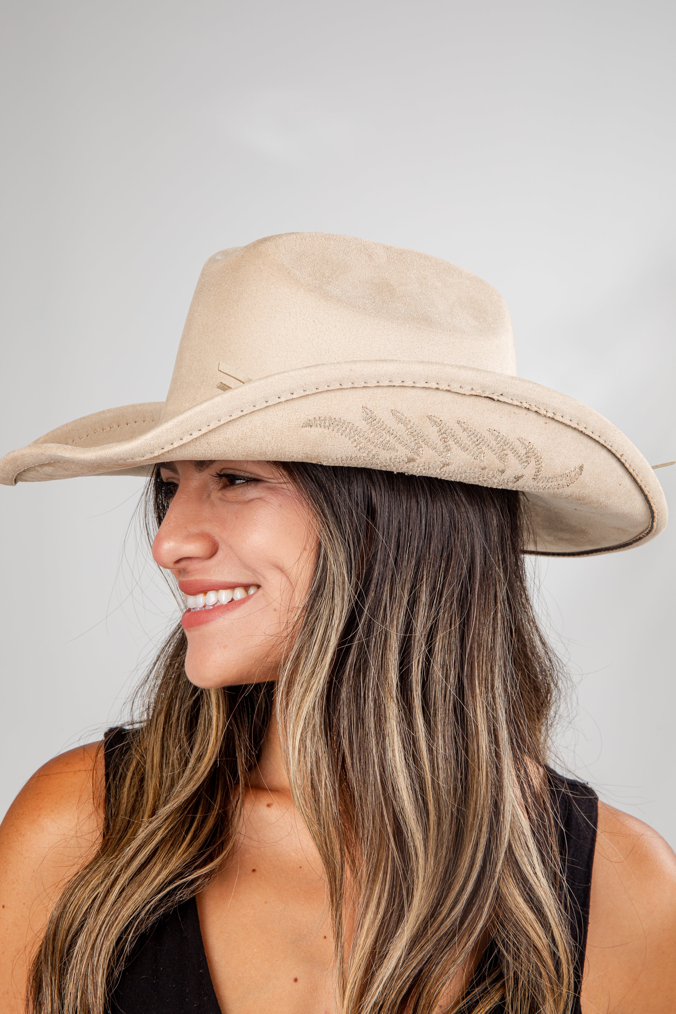 Woman wearing a beige wide-brimmed hat against a plain background
