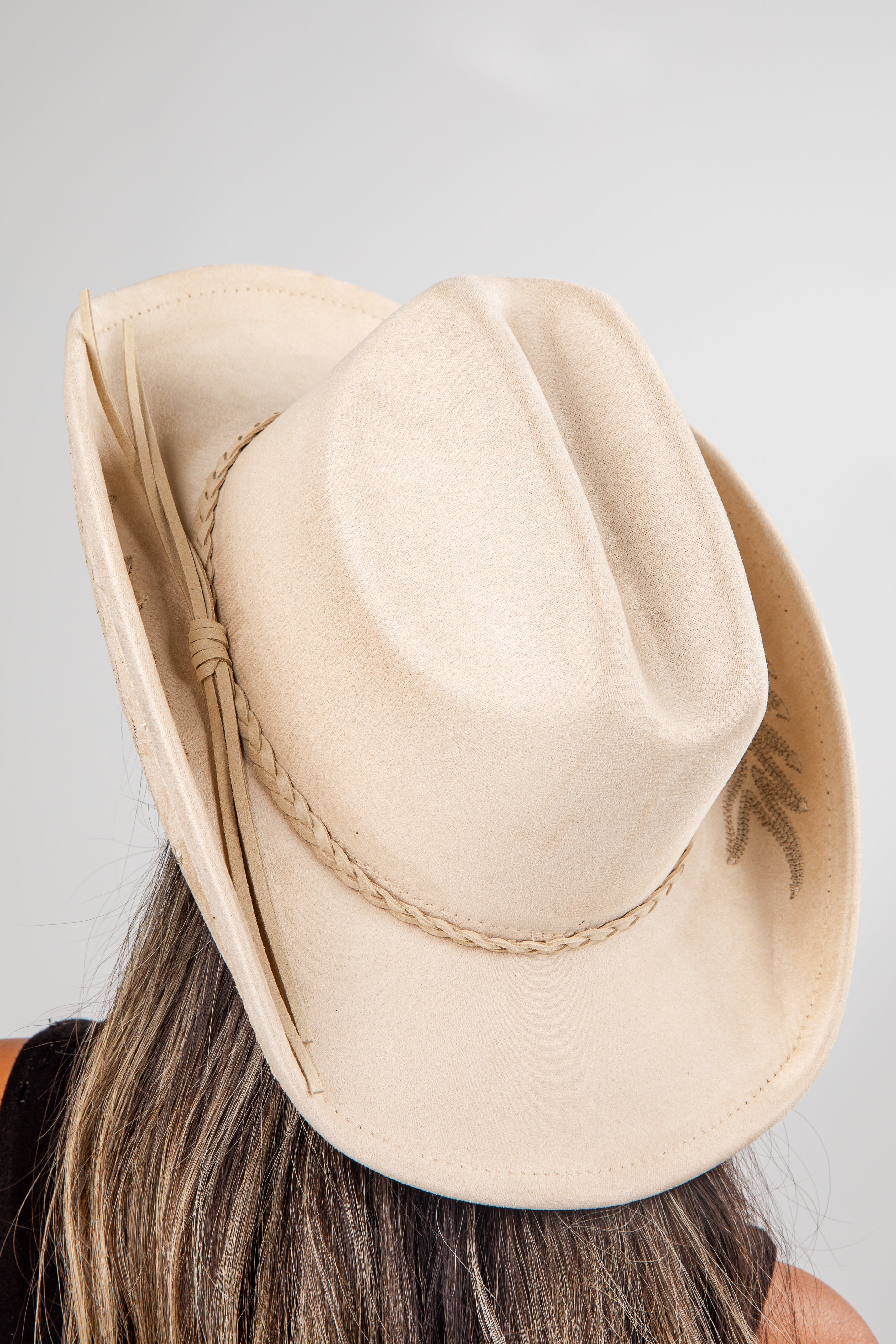 Beige fedora hat worn by a person with a plain background