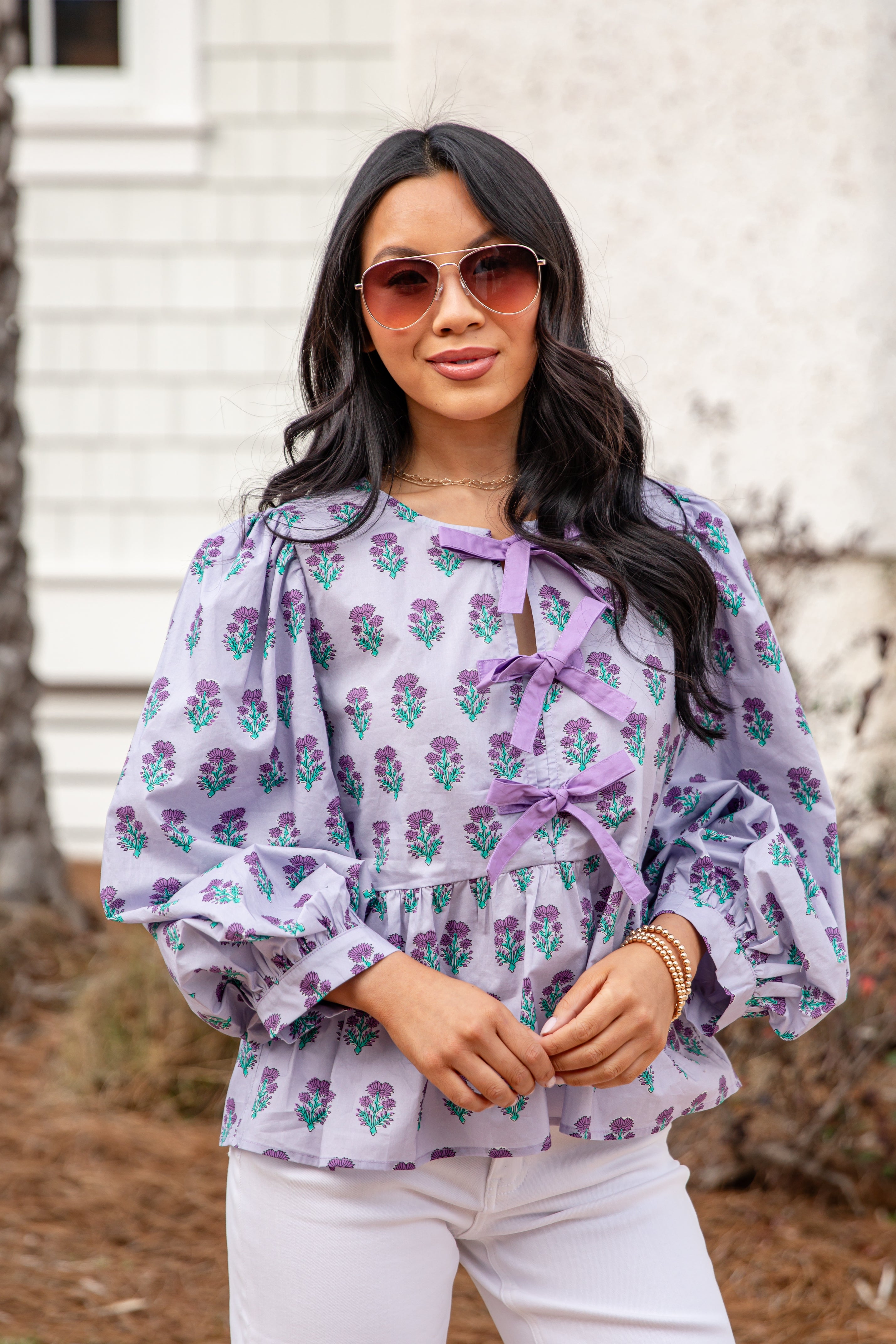 Woman wearing a floral blouse with ruffled sleeves and a bow tie, standing outdoors.