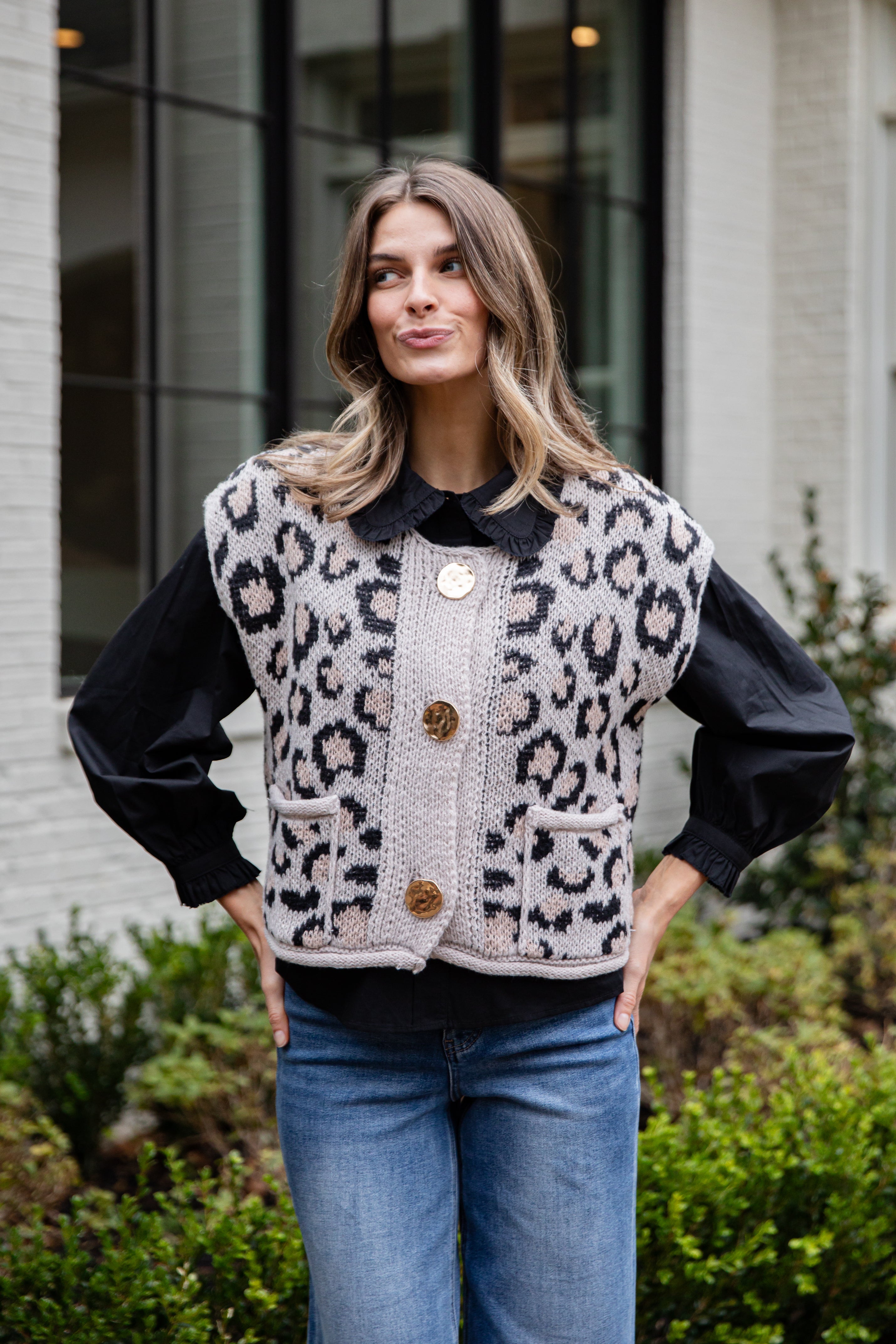 Woman wearing a leopard print vest with a black shirt and blue jeans, standing outdoors.