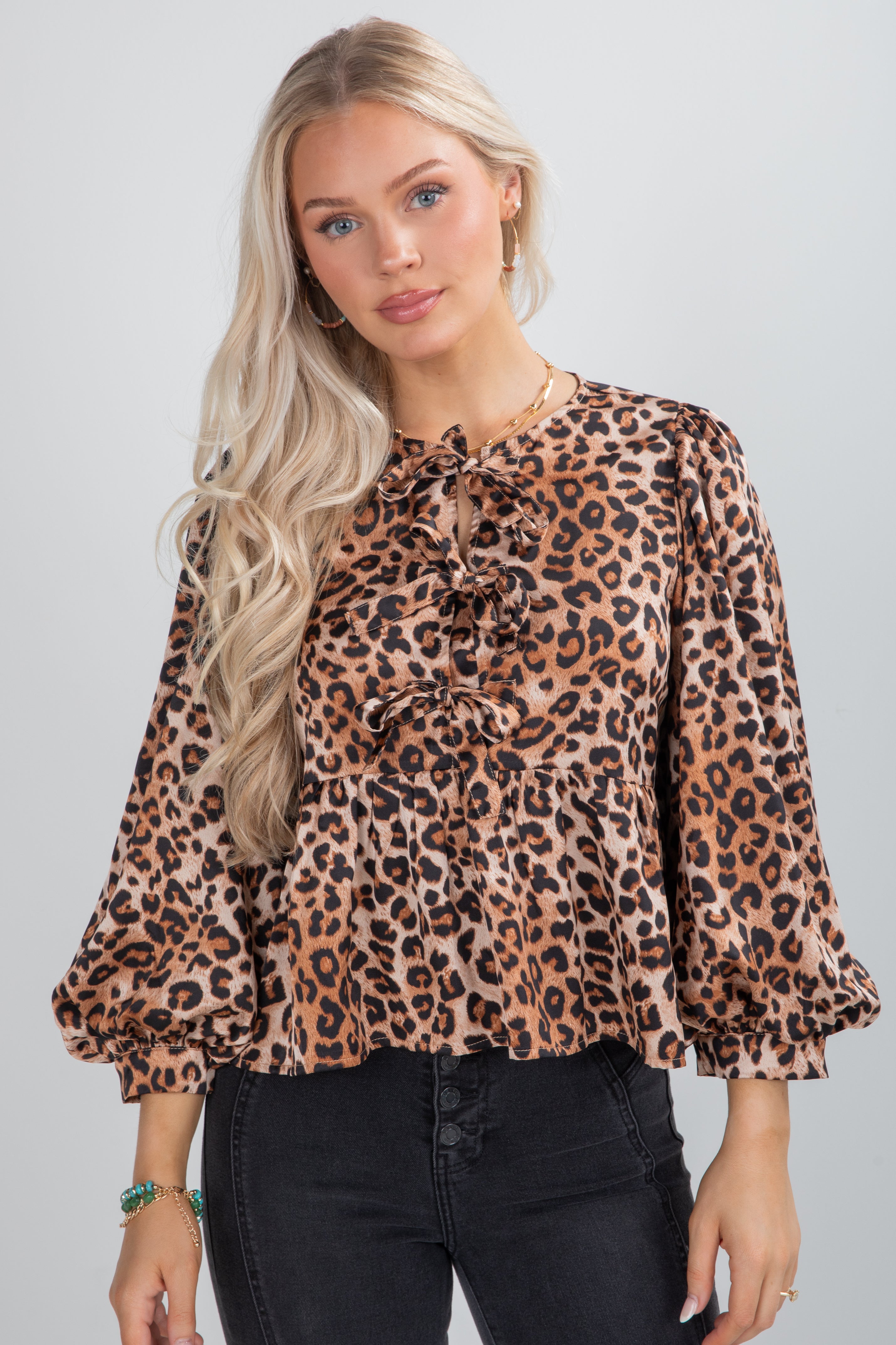 Woman wearing a leopard print blouse with long sleeves on a plain background
