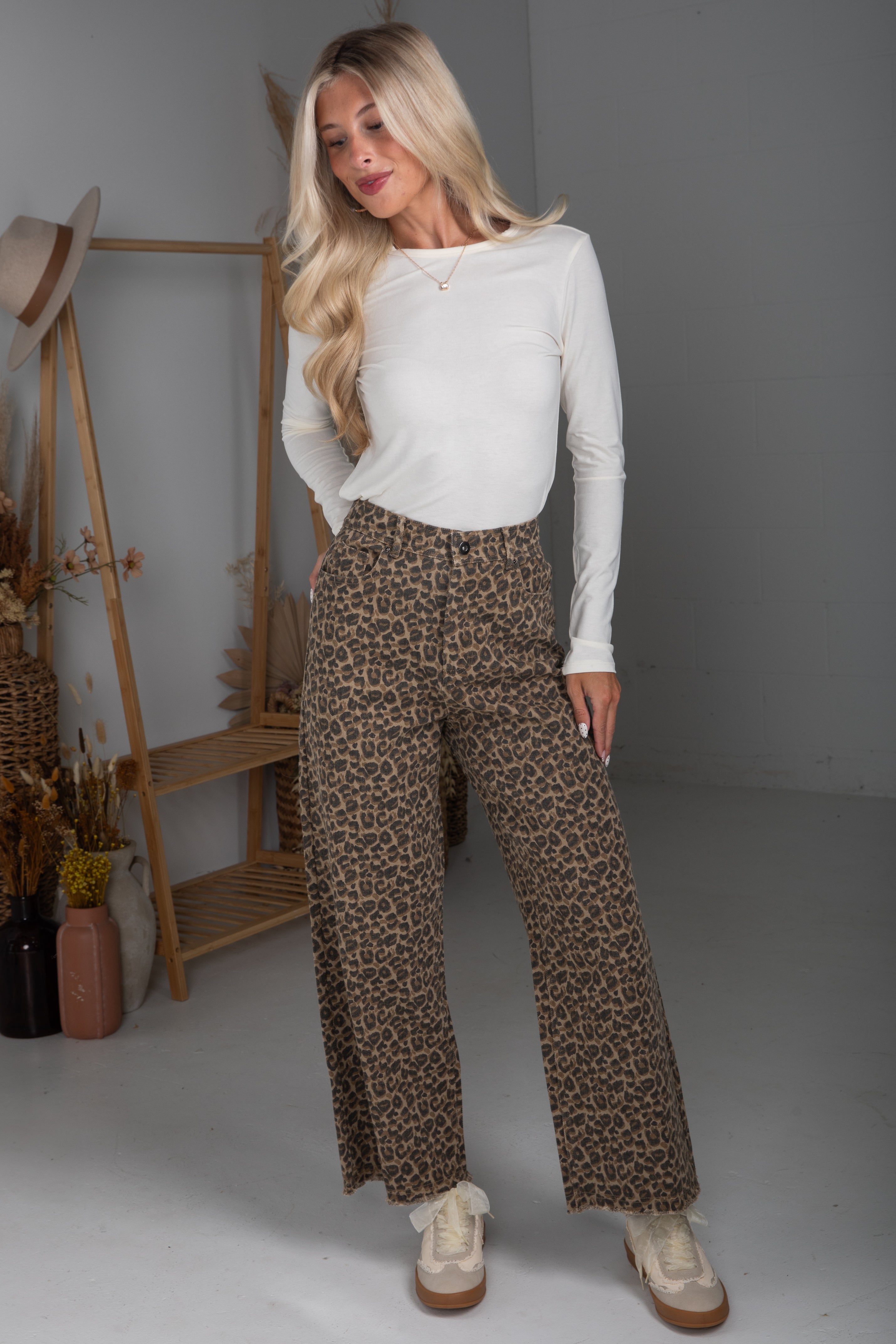 Woman wearing a white long-sleeve top and leopard print pants in a neutral setting