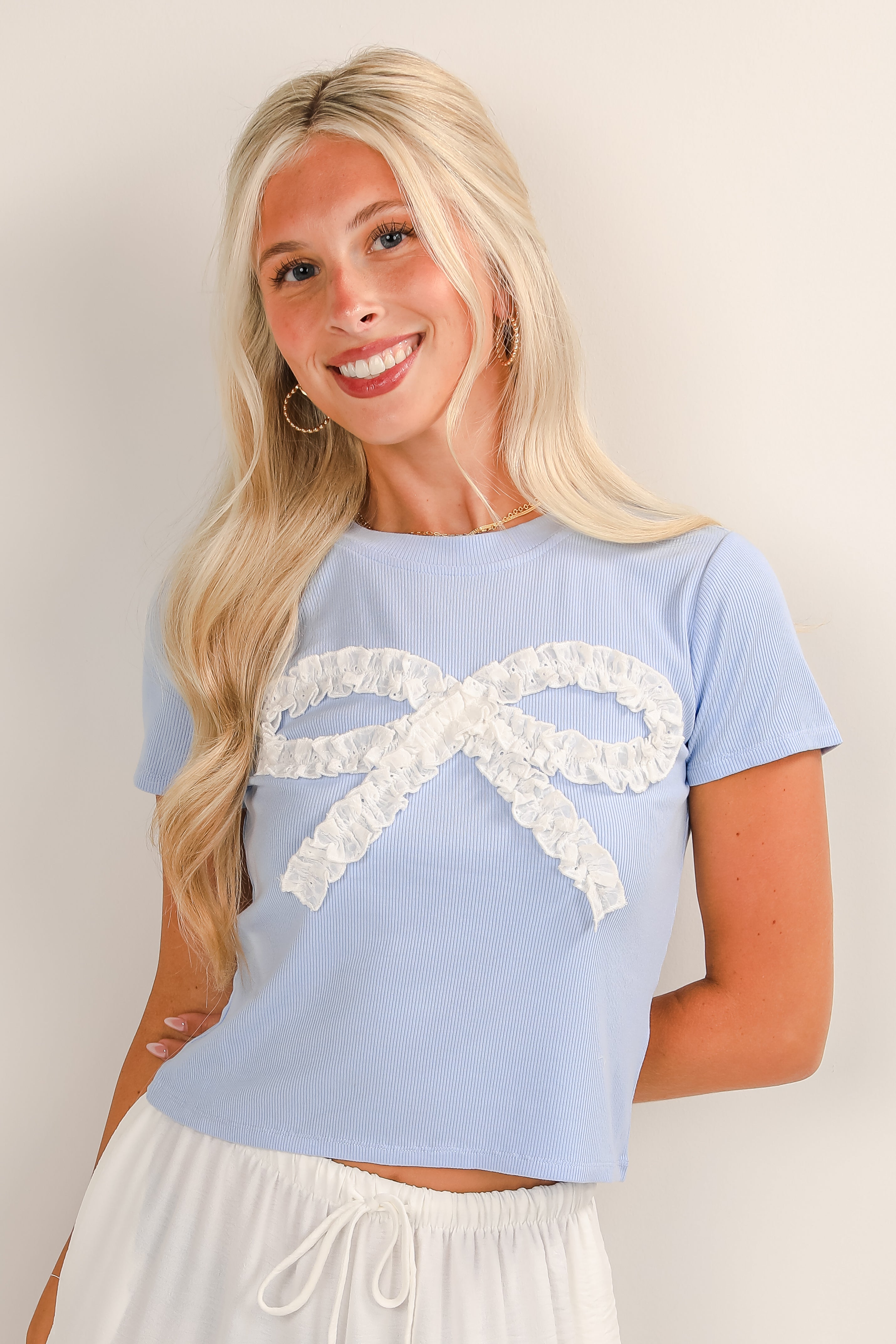 Woman wearing a light blue top with a white bow design on a plain background