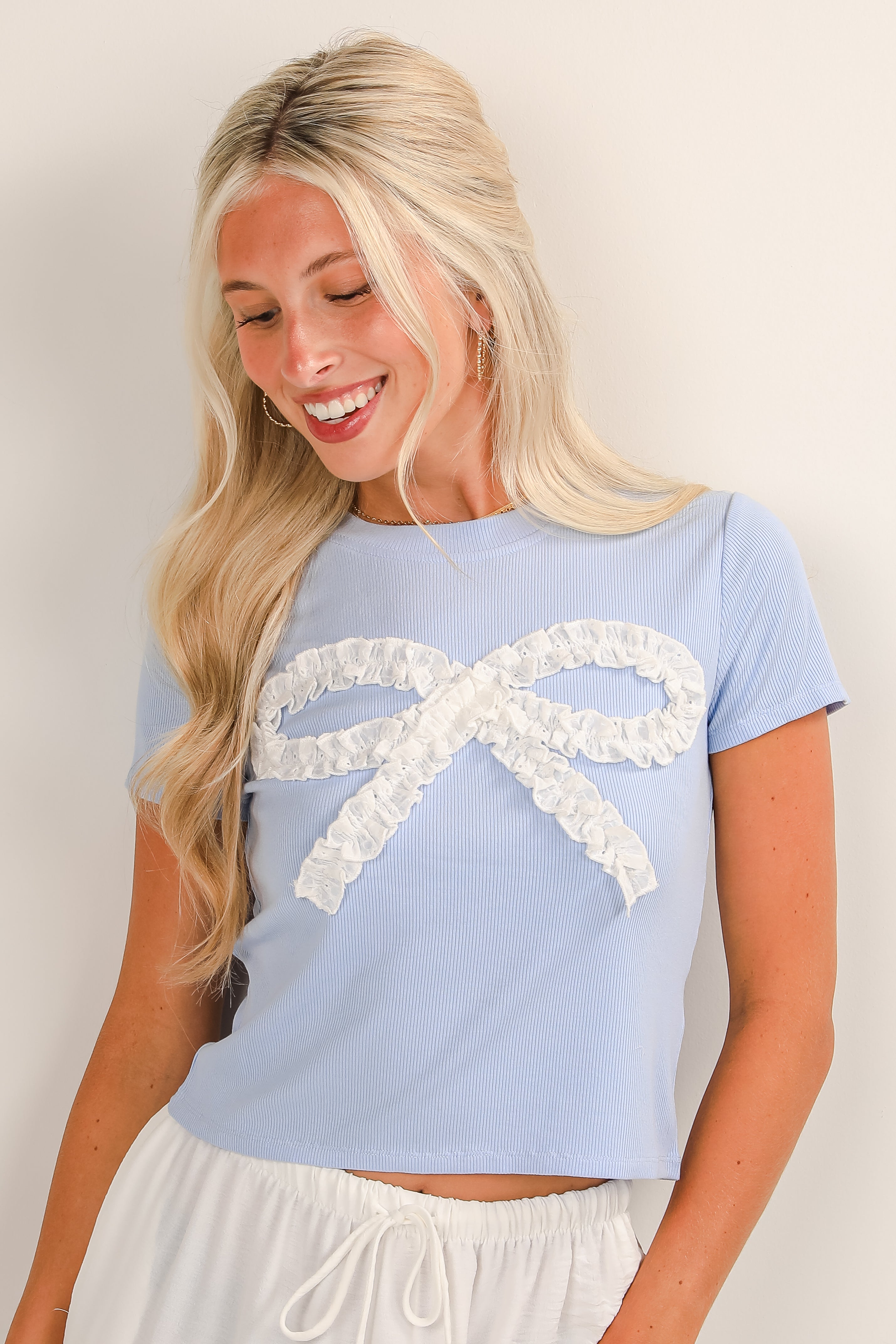 Woman wearing a light blue t-shirt with a white lace bow design on a plain background