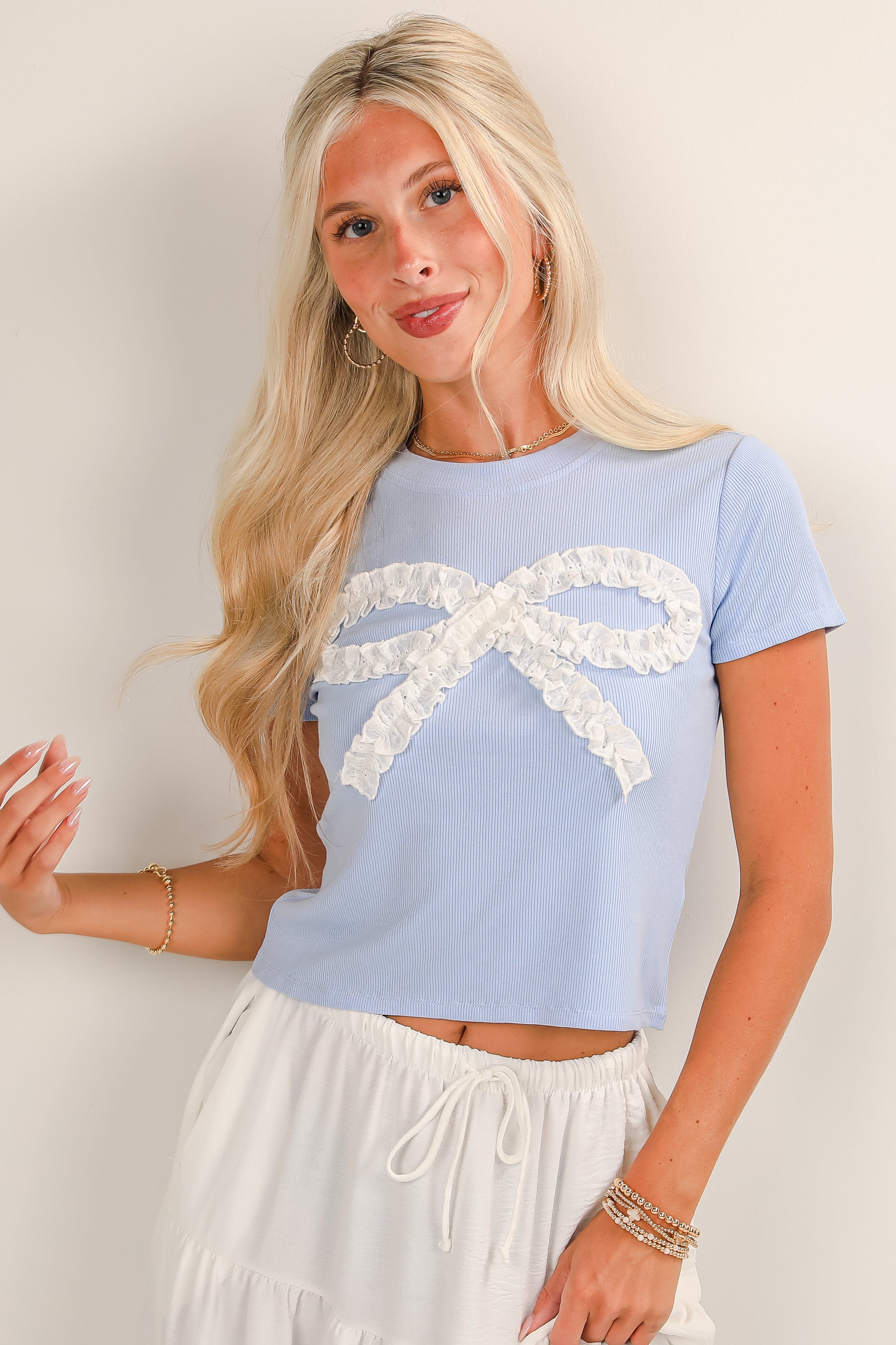 Woman wearing a light blue top with a white lace bow design on a plain background