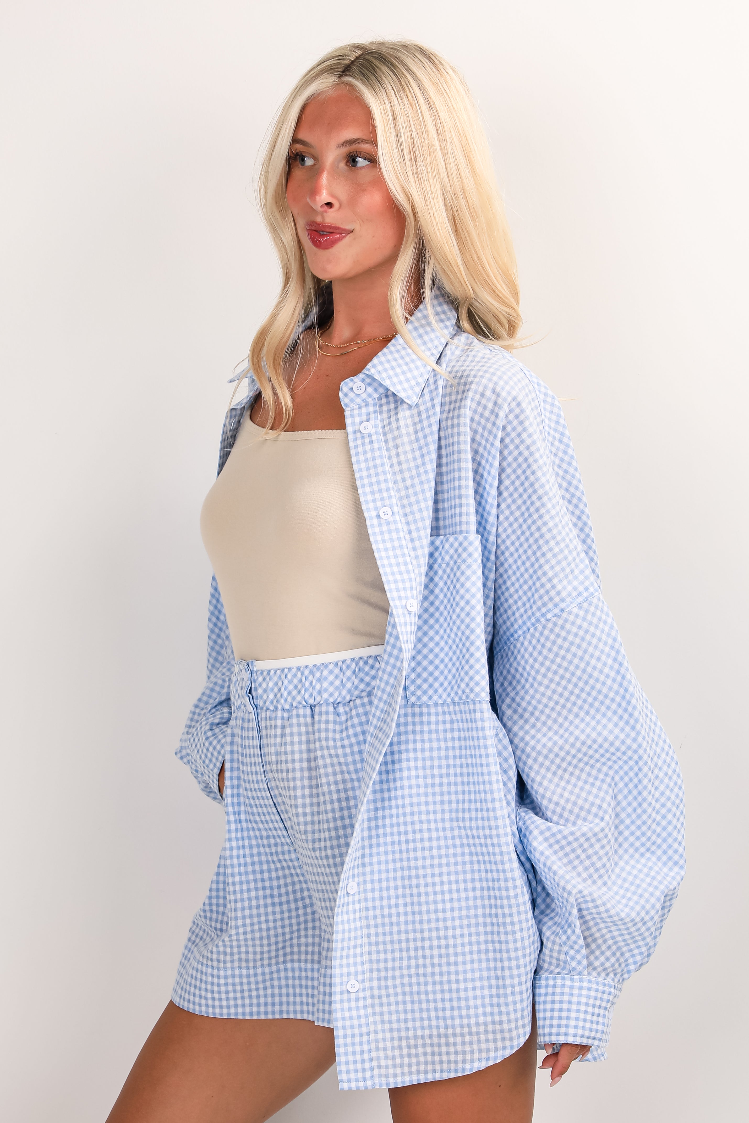 Woman wearing a light blue checkered shirt and shorts on a plain background