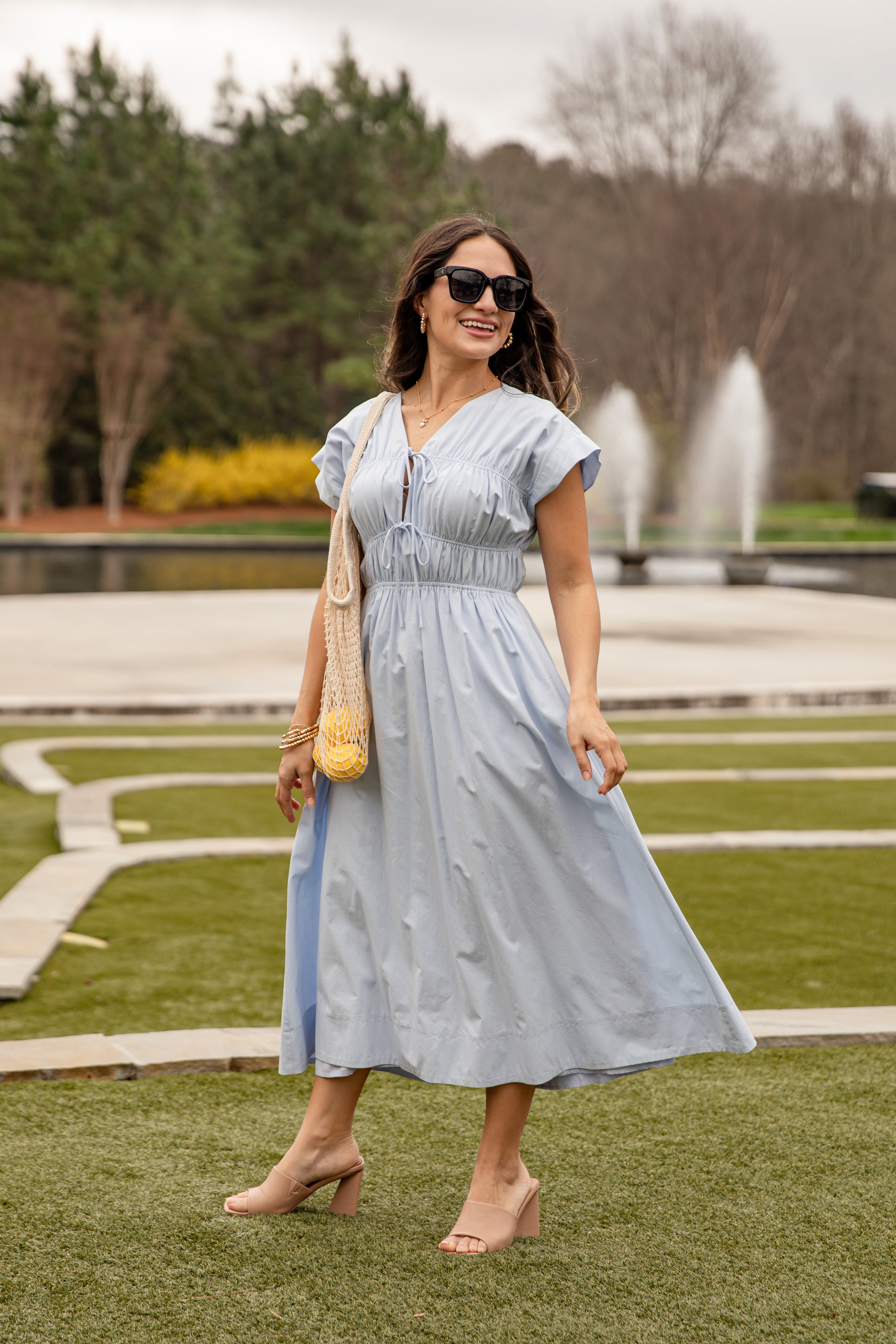 Woman in a light blue dress standing in a park with a fountain in the background