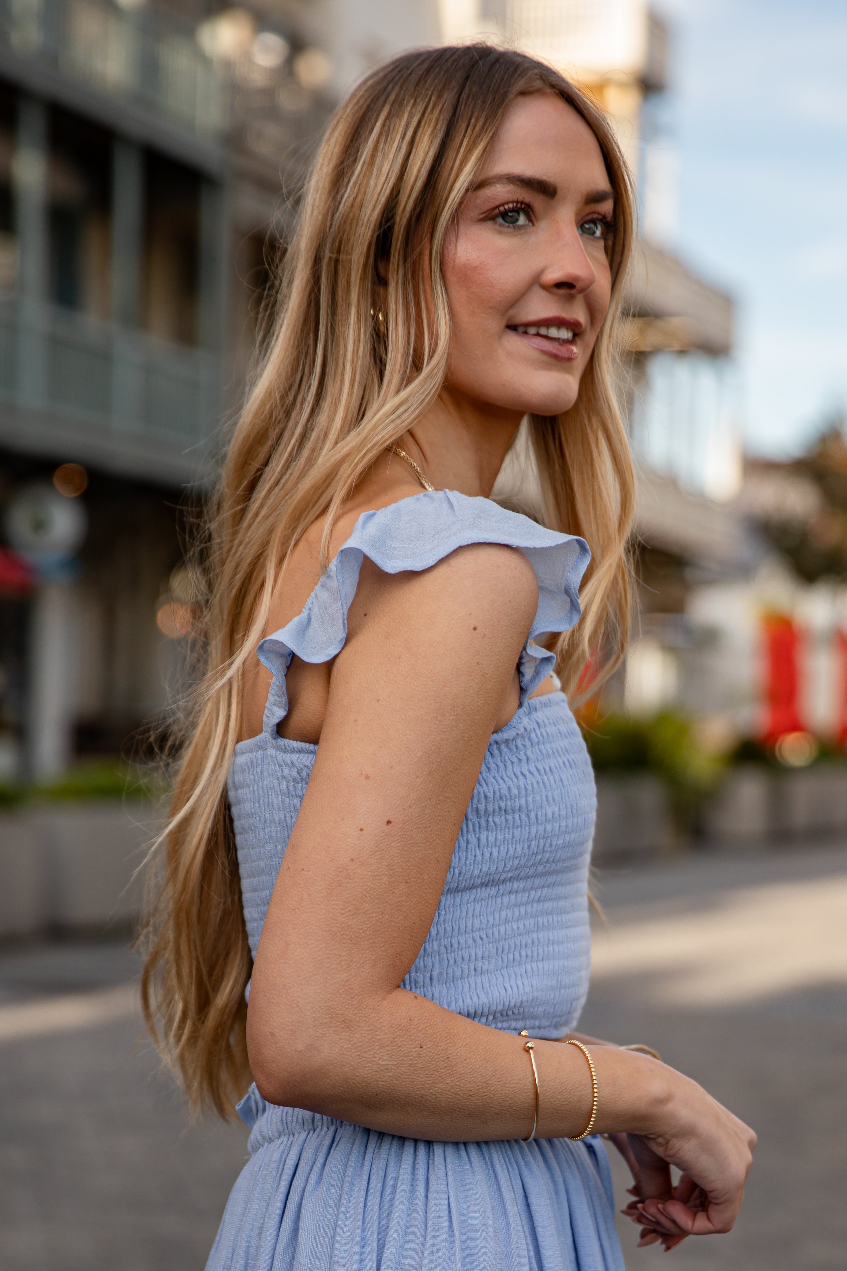Woman in a light blue dress with ruffled shoulders standing outdoors.