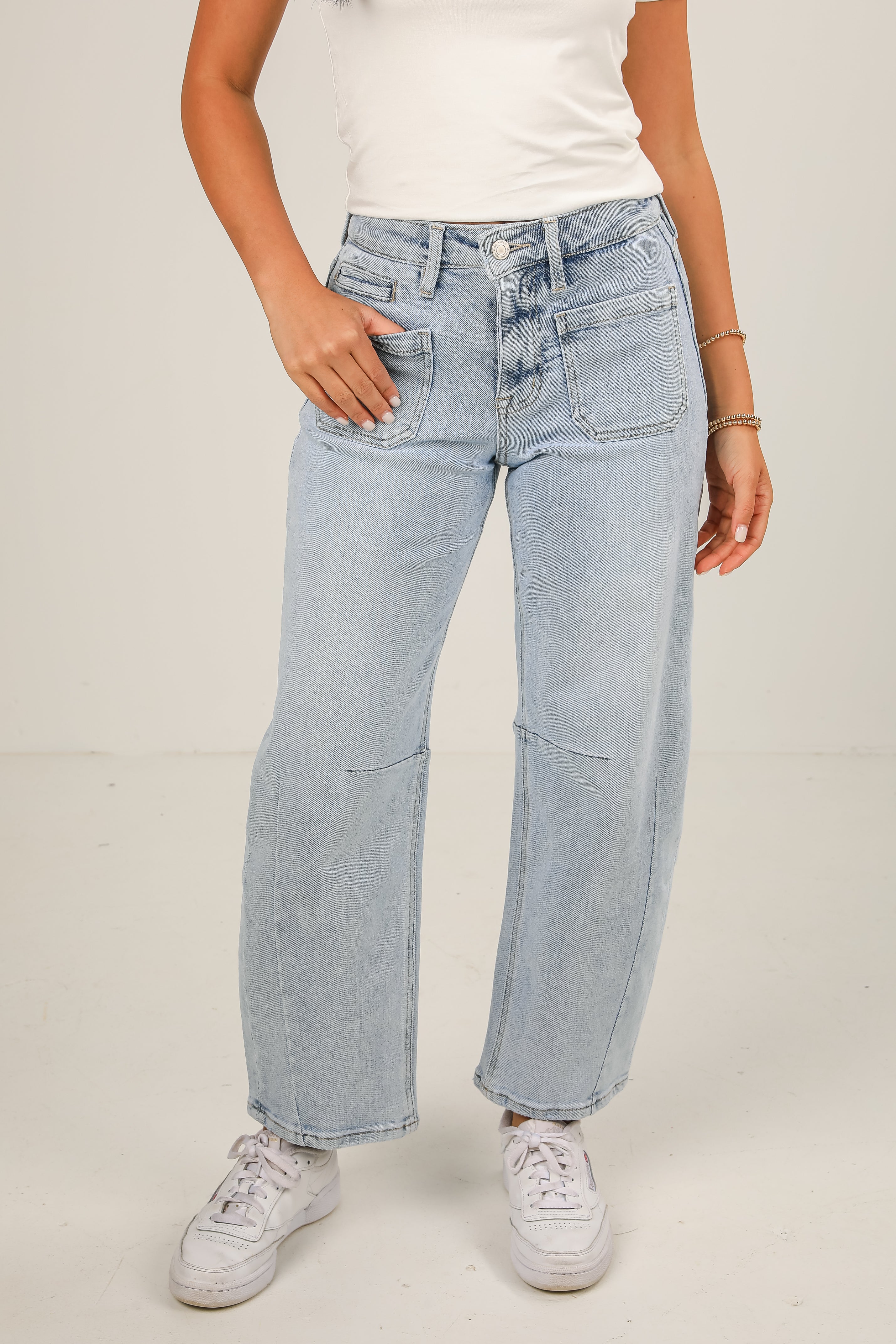 Person wearing light blue jeans and white sneakers on a plain background