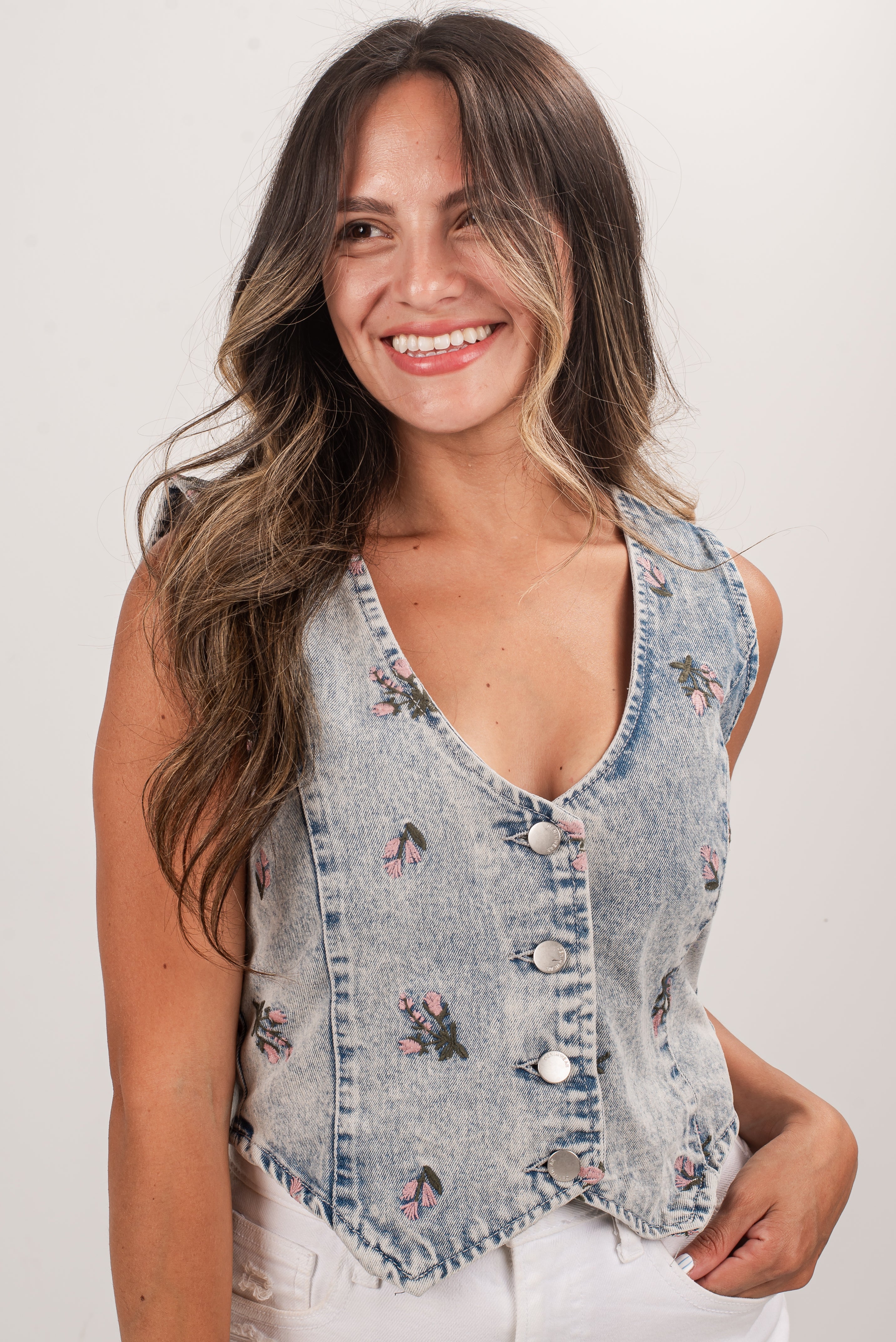 Woman wearing a denim vest with floral embroidery on a plain background