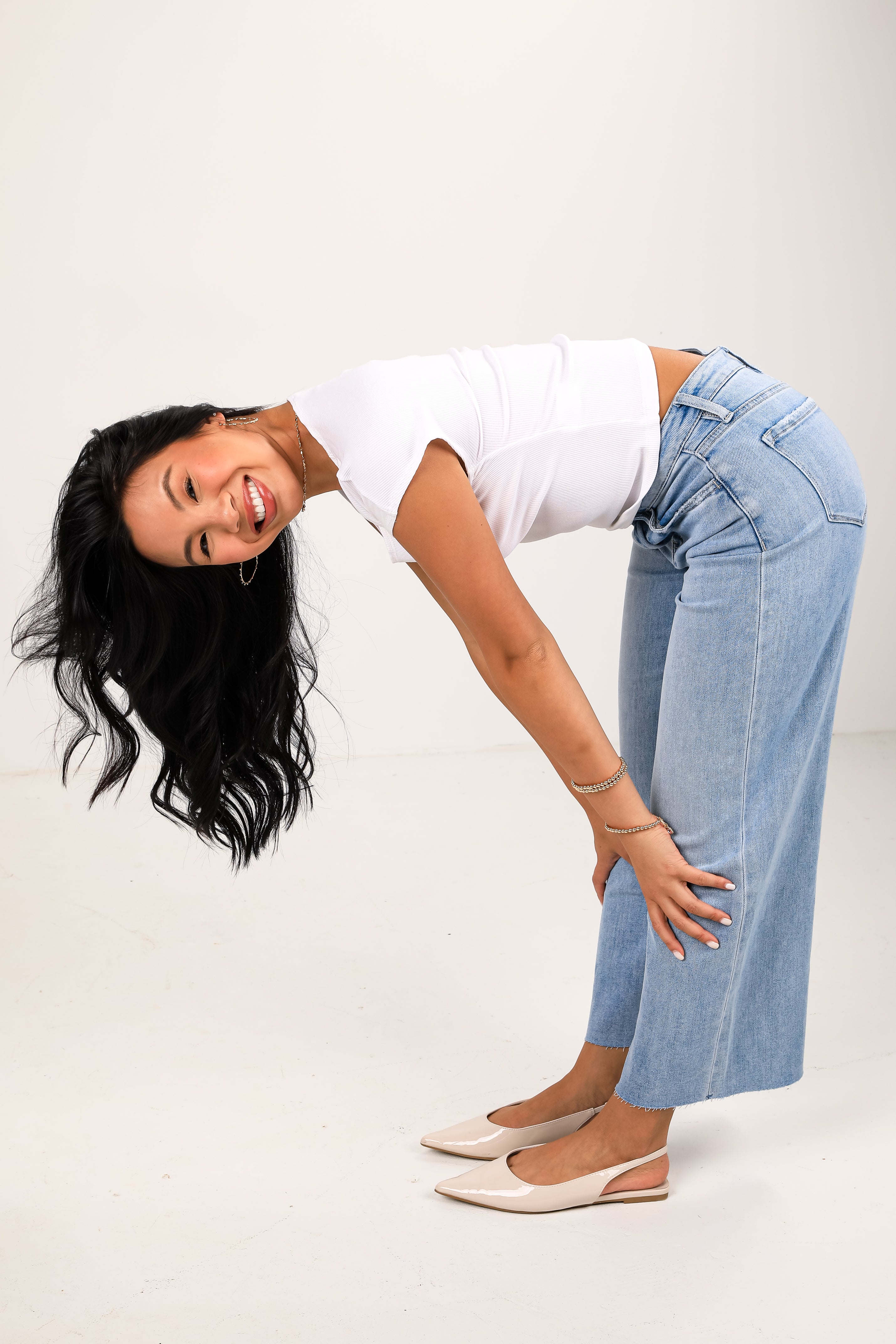 Woman wearing a white top and blue jeans posing against a plain background