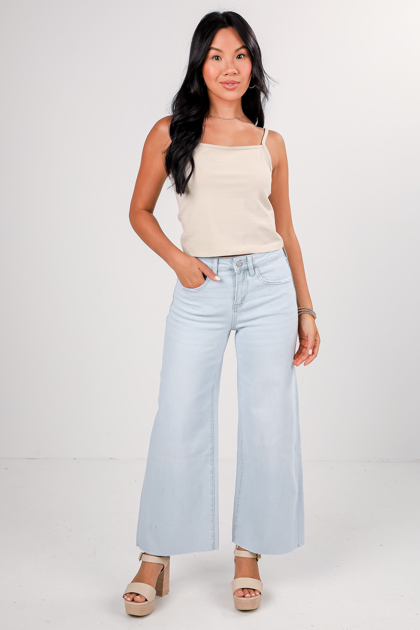 Woman wearing a beige tank top and light blue jeans on a white background