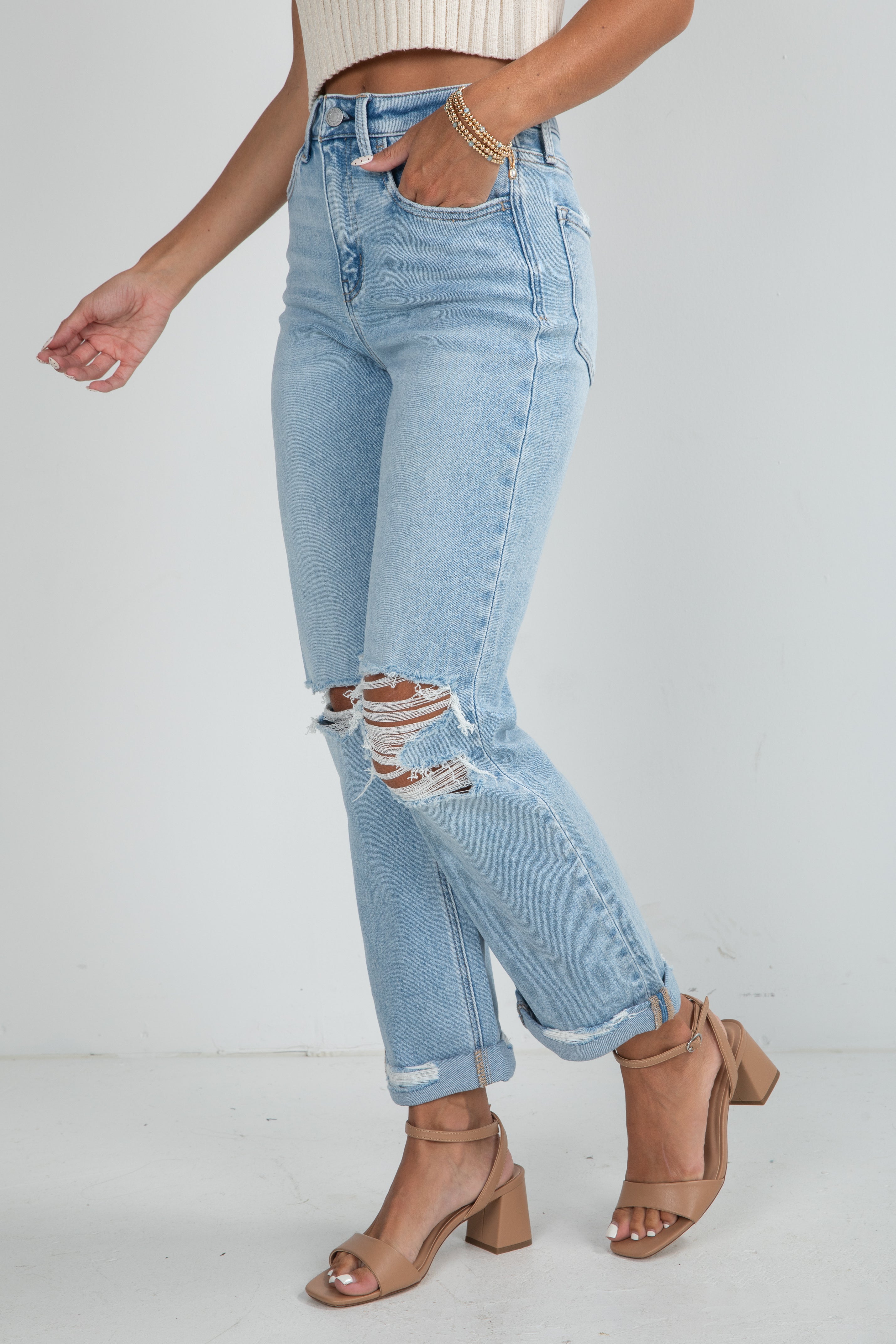Person wearing light blue ripped jeans and brown sandals on a white background
