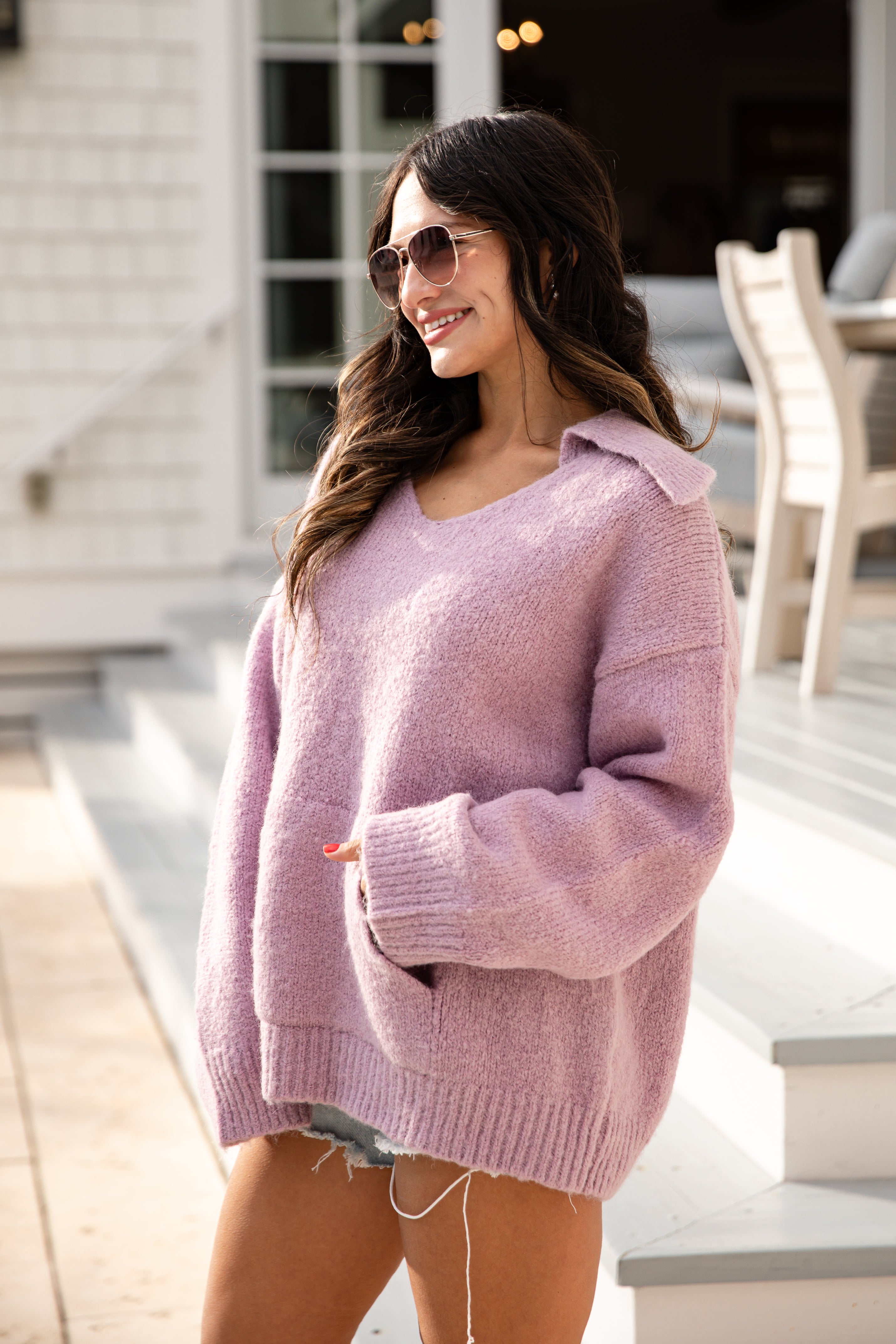 Woman wearing a pink sweater standing outdoors on a patio.