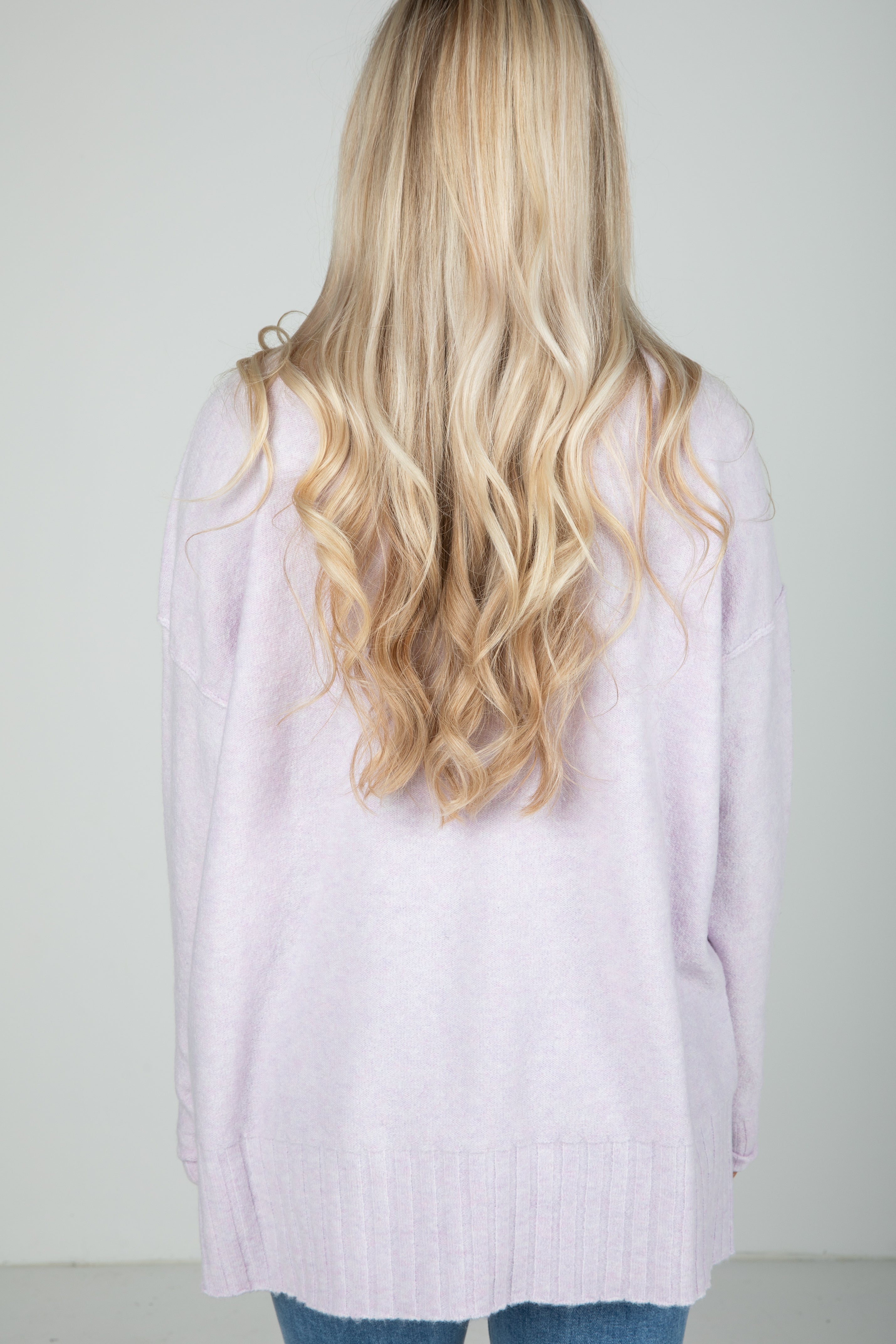 Person wearing a light purple cardigan with long, wavy blonde hair.