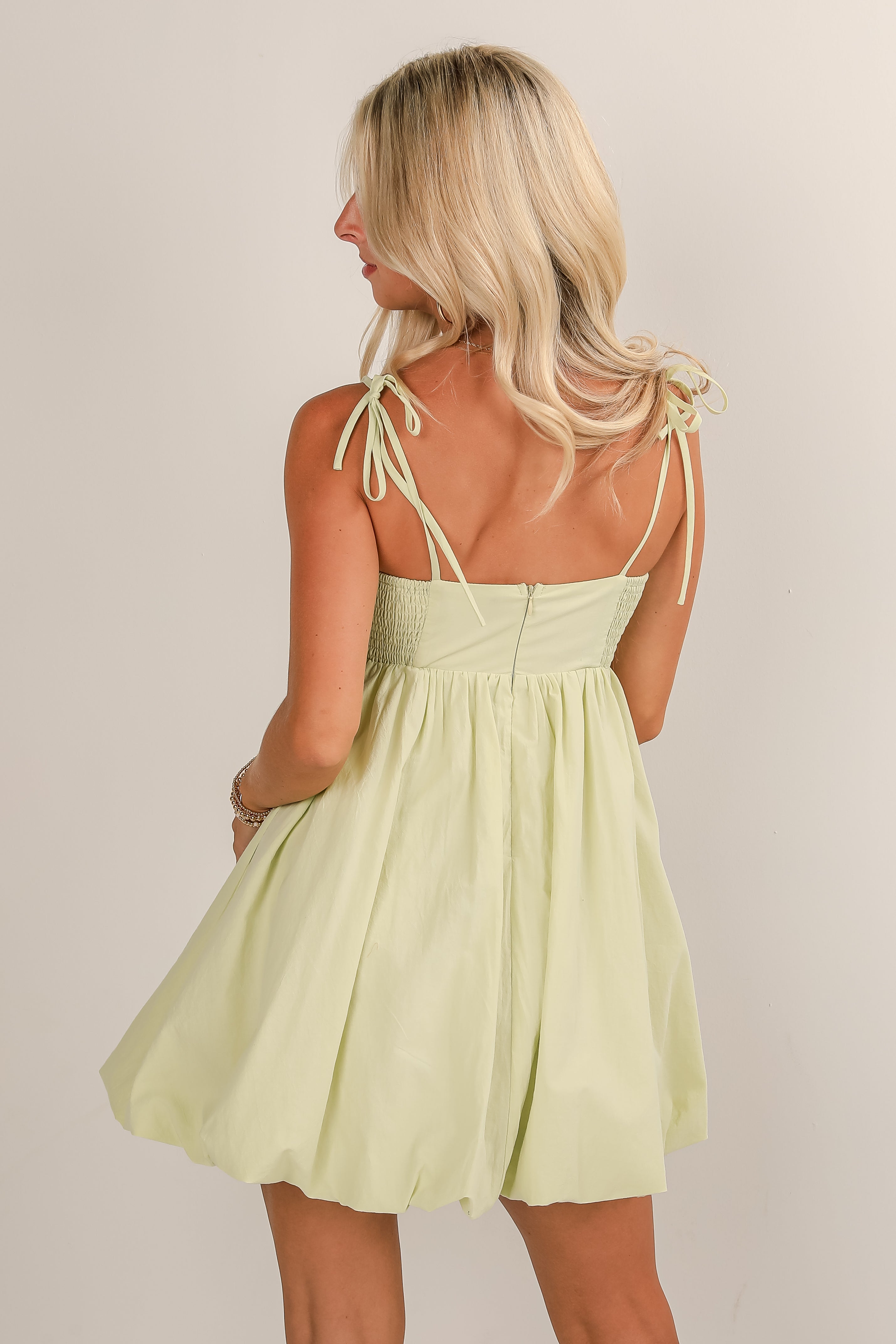 Woman wearing a light green dress with thin straps on a plain background