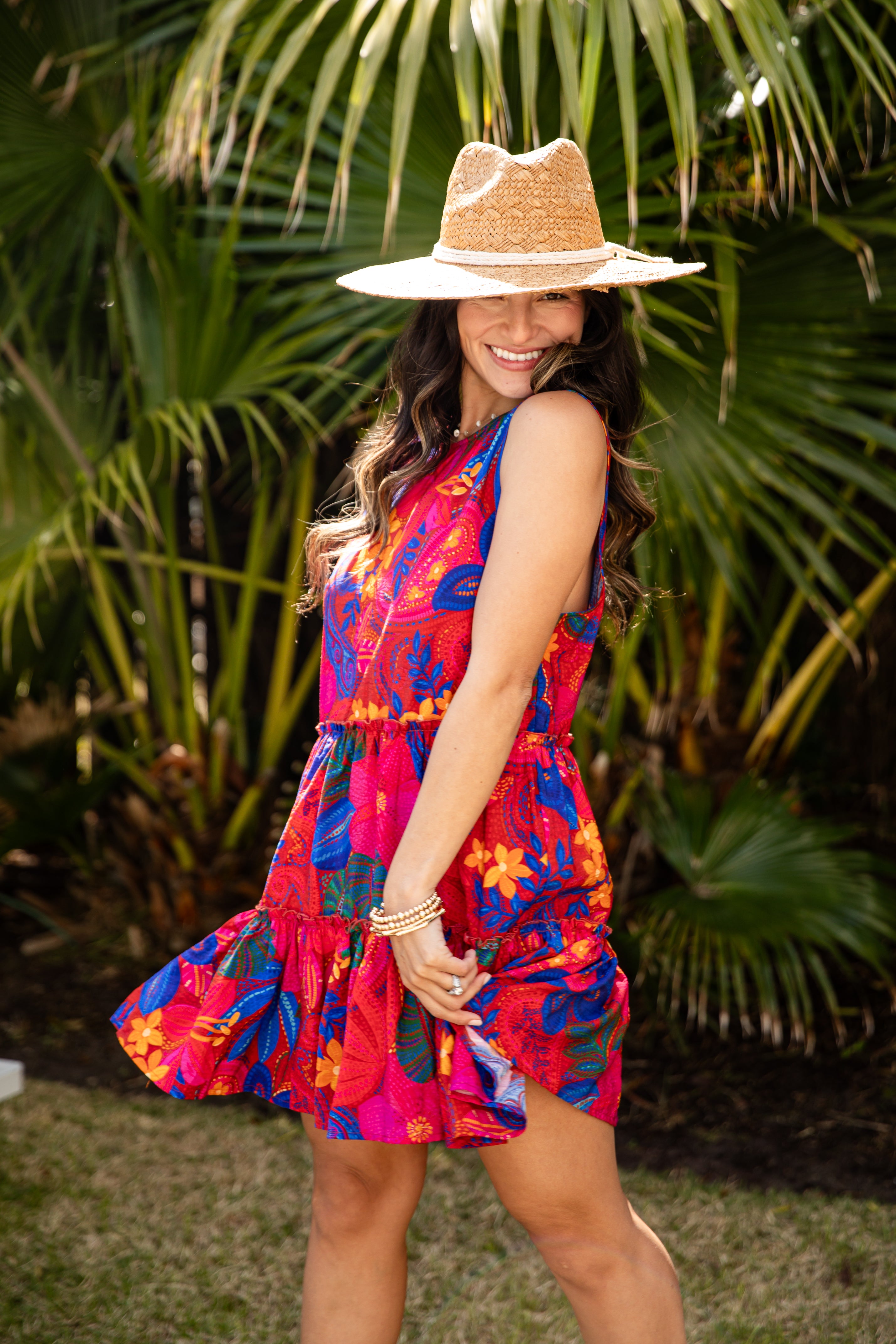 Woman in a colorful dress and straw hat standing in front of tropical plants