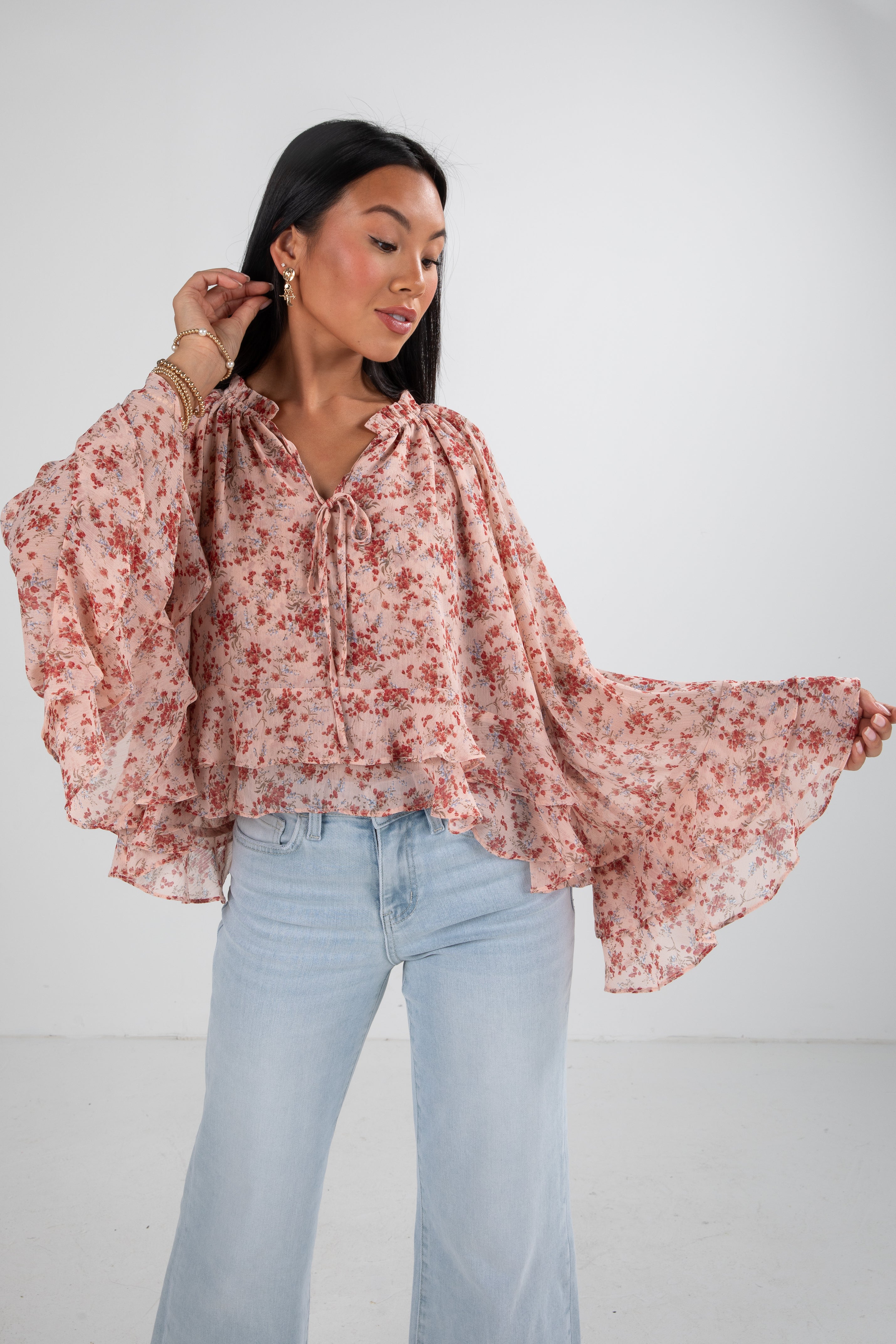 Woman wearing a floral blouse and light blue jeans against a white background